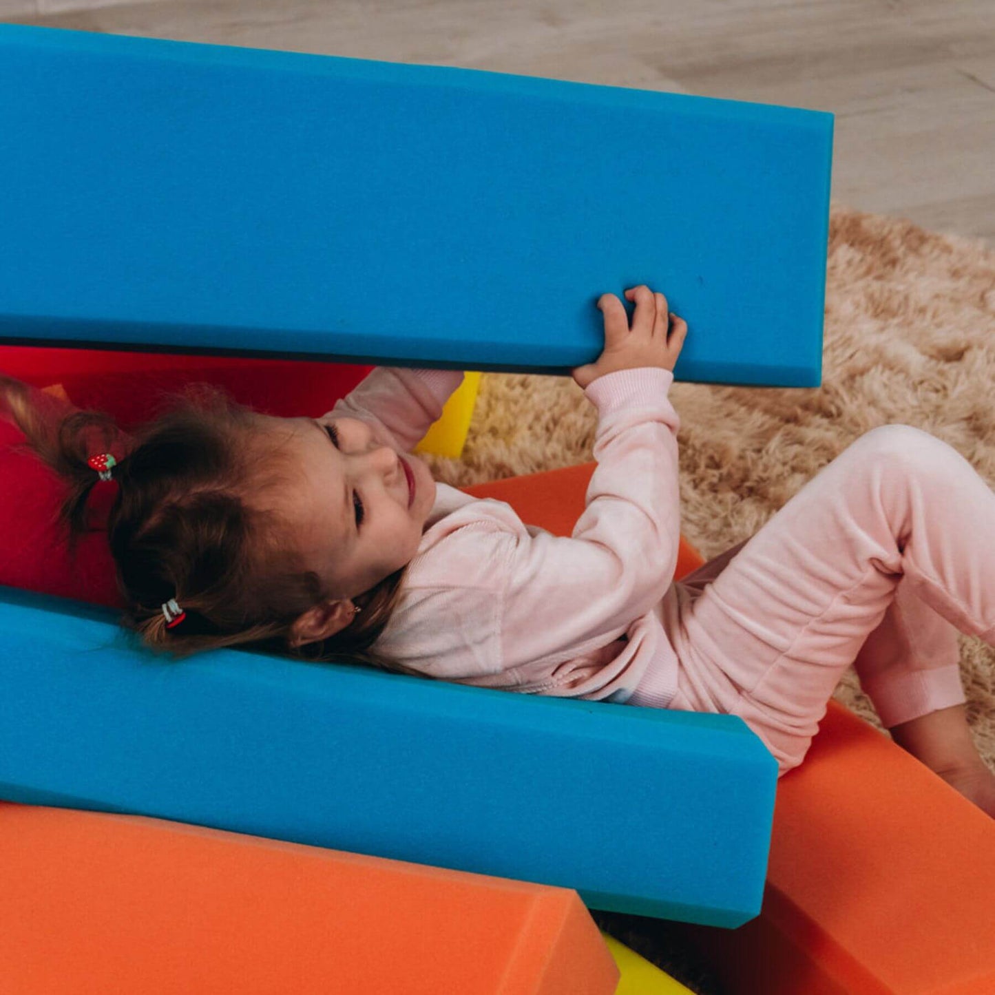 Child playing on colorful foam blocks on a wooden floor