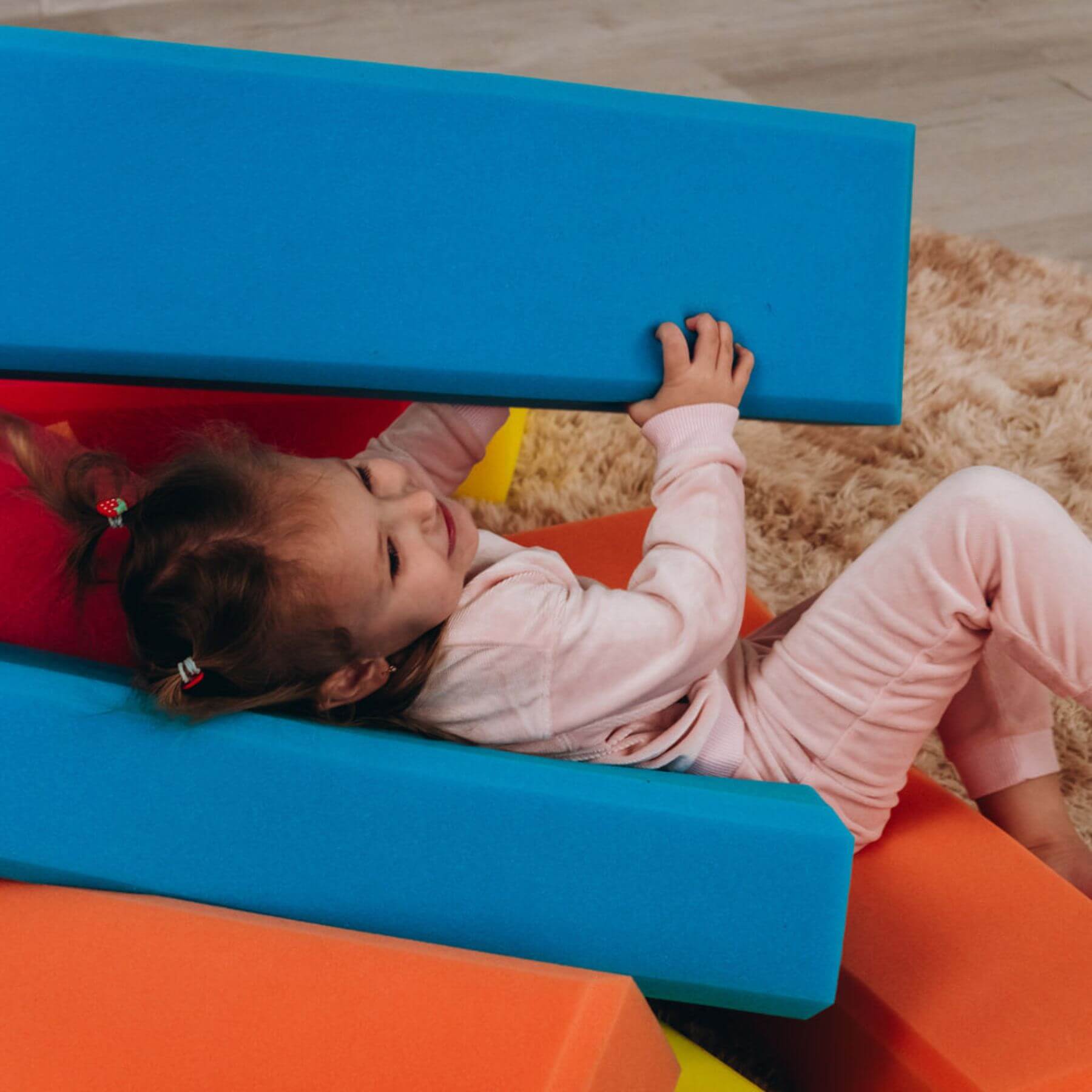 Child playing on colorful foam blocks on a wooden floor