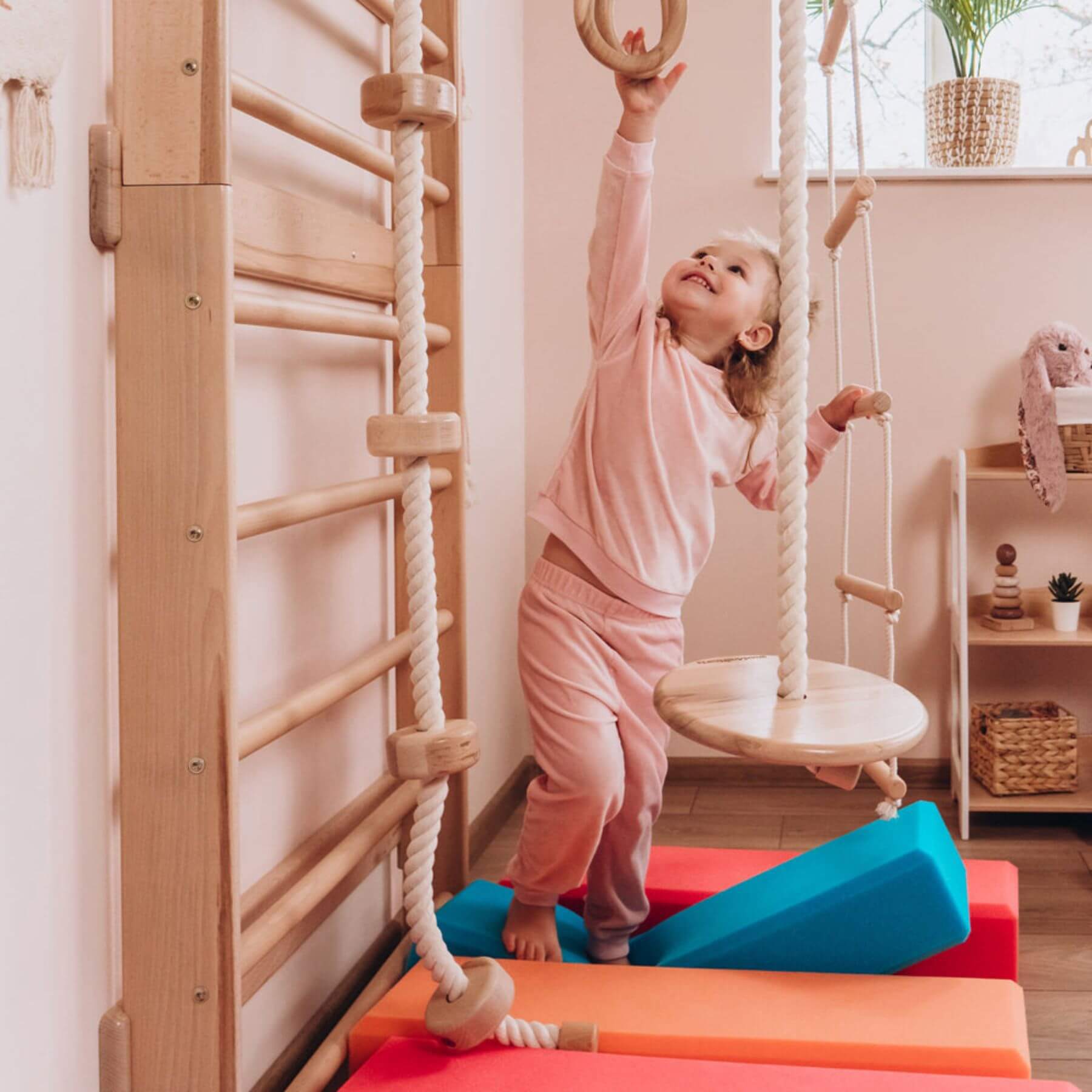 Child playing on a wooden climbing frame with colorful platforms in a home setting.