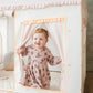 Child in a floral dress standing behind a white curtain with pink trim.