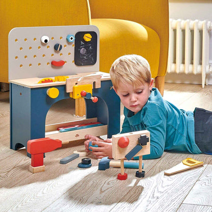 Child playing with Tender Leaf Table Top Tool Bench in a room with a yellow chair.