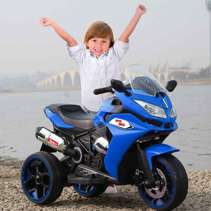Child with arms raised next to Tamco 12V Kids Electric Ride On Motorcycle - Blue by a water body