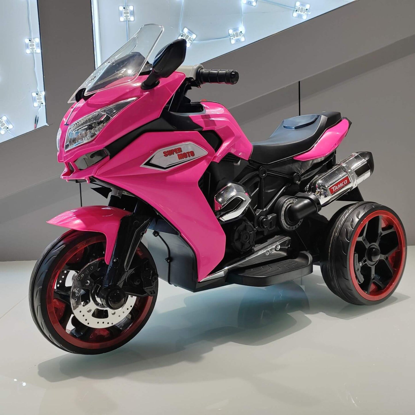 Tamco 12V Kids Electric Ride On Motorcycle - Pink on a reflective surface with a neutral background