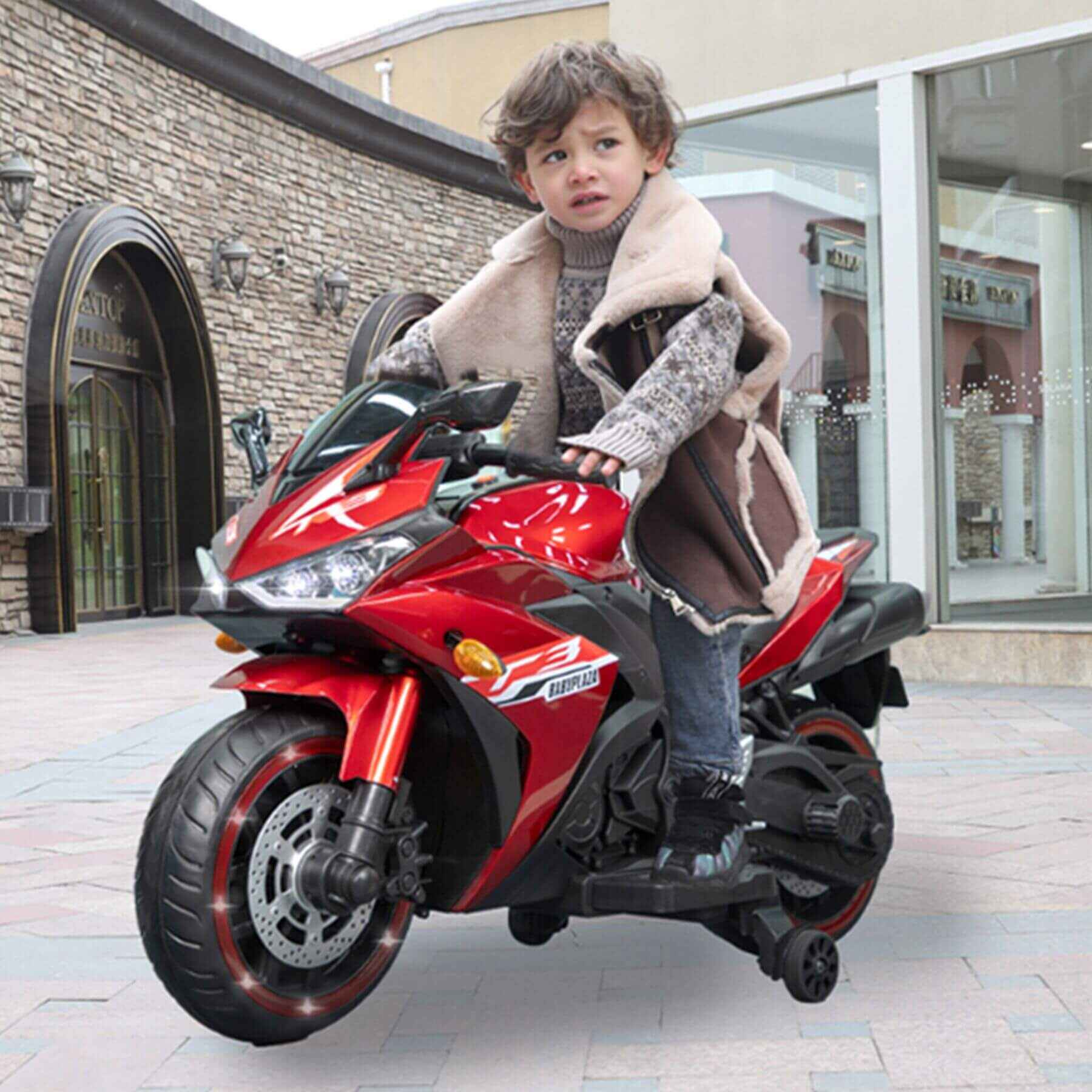 Child on Tamco Kids 12V Motorcycle with Training Wheels - Red in front of a building