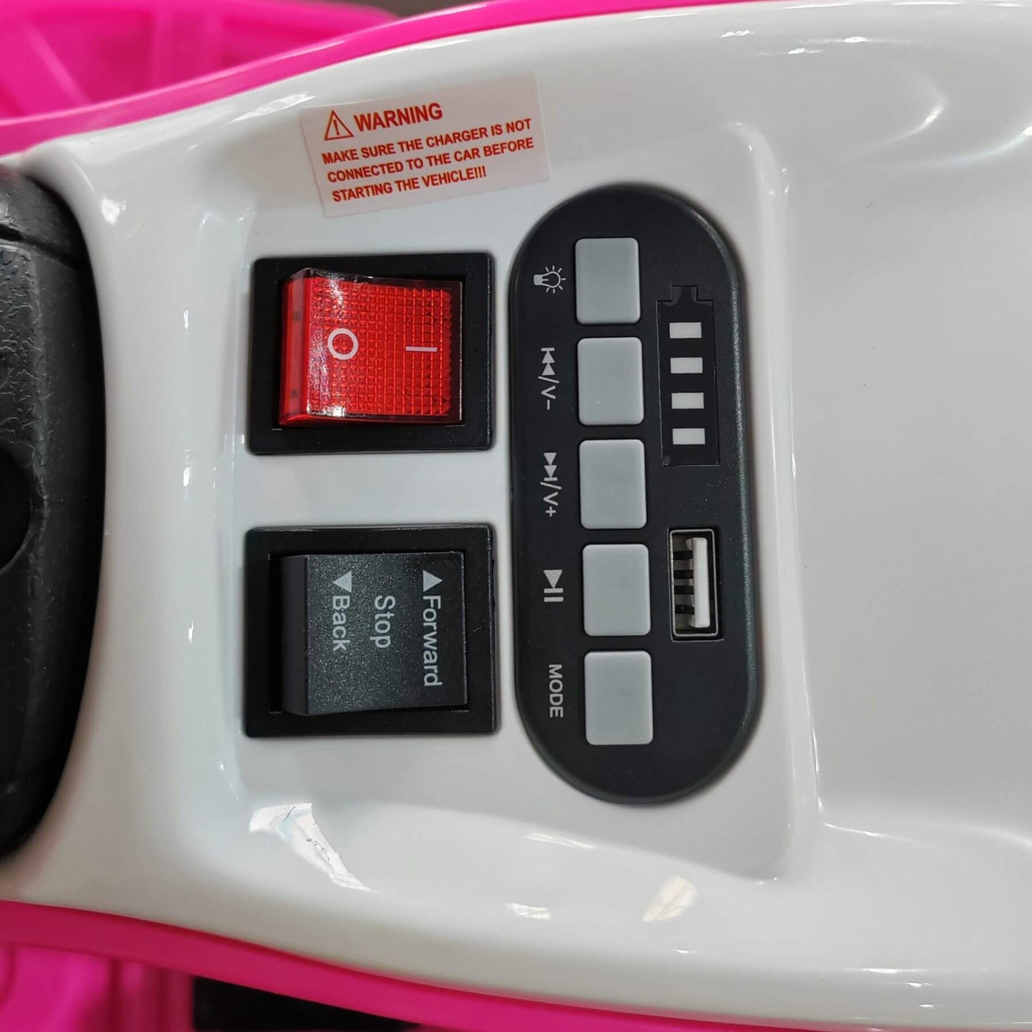 Control panel with buttons and warning label on a pink and white toy car.