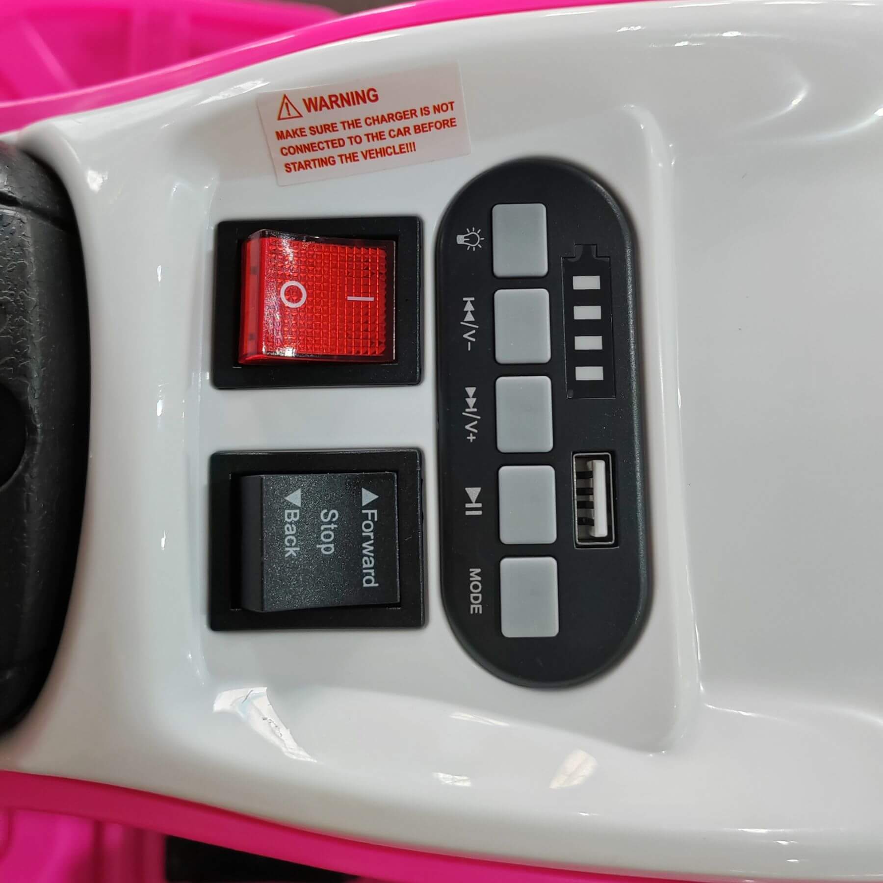 Control panel with buttons and warning label on a pink and white toy car.