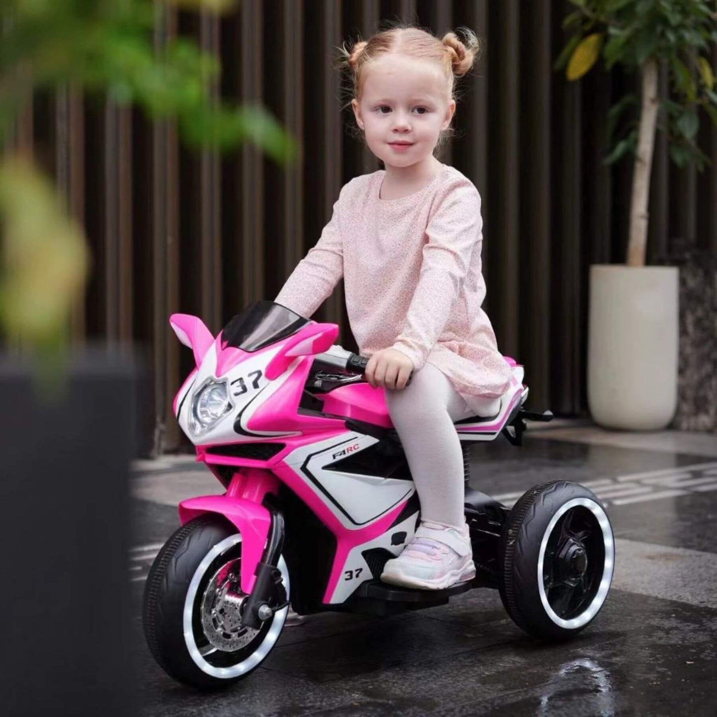 Child sitting on Tamco 6V Kids Electric Motorcycle - Pink outdoors.