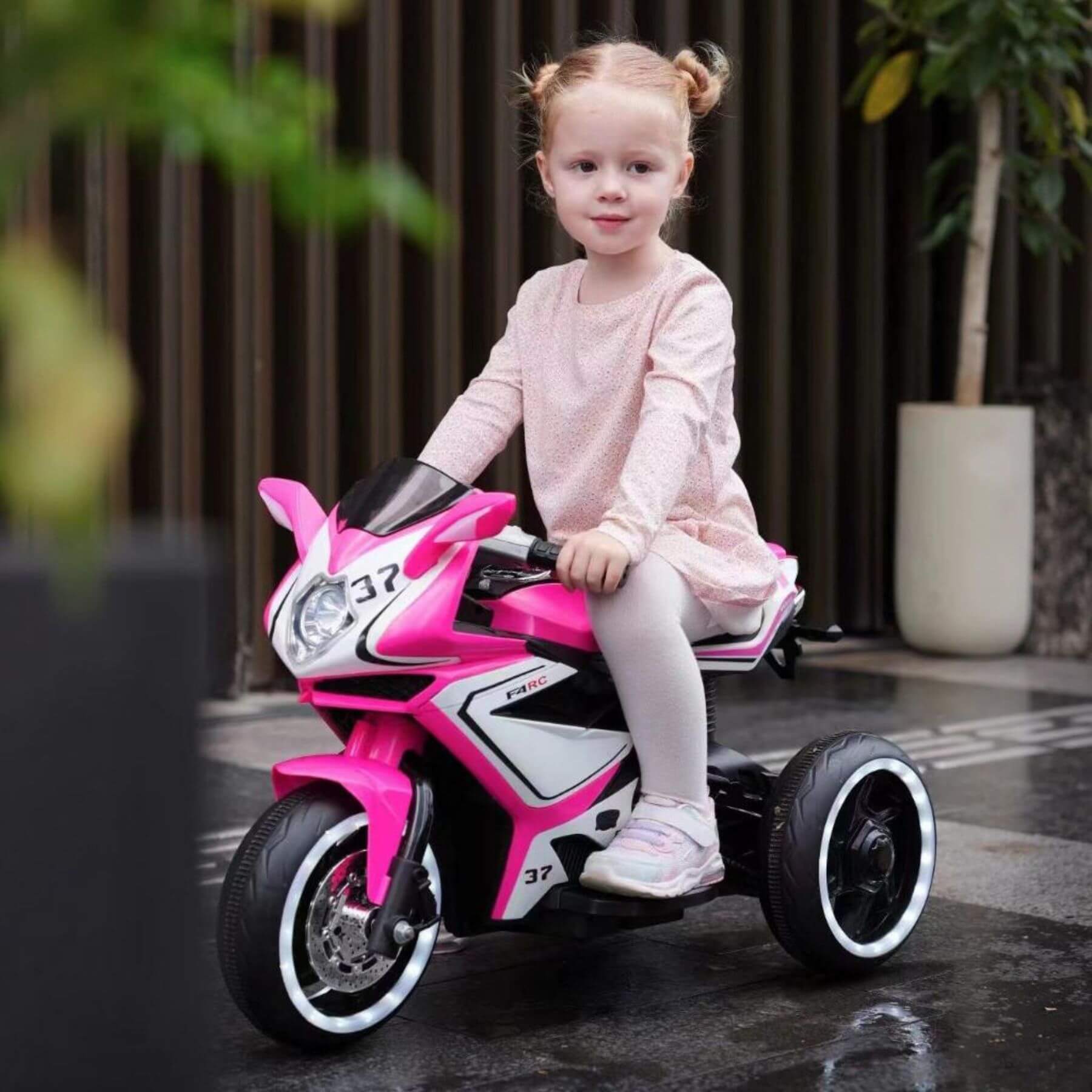 Child sitting on Tamco 6V Kids Electric Motorcycle - Pink outdoors.