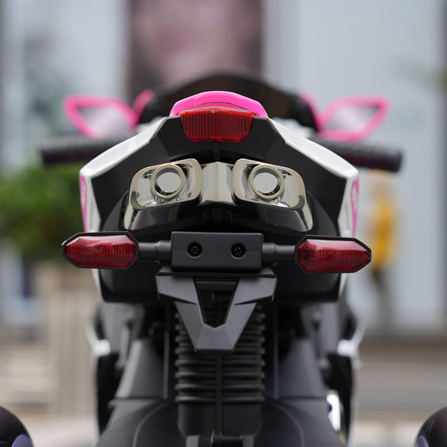 Close-up of Child sitting on Tamco 6V Kids Electric Motorcycle - Pink with blurred background