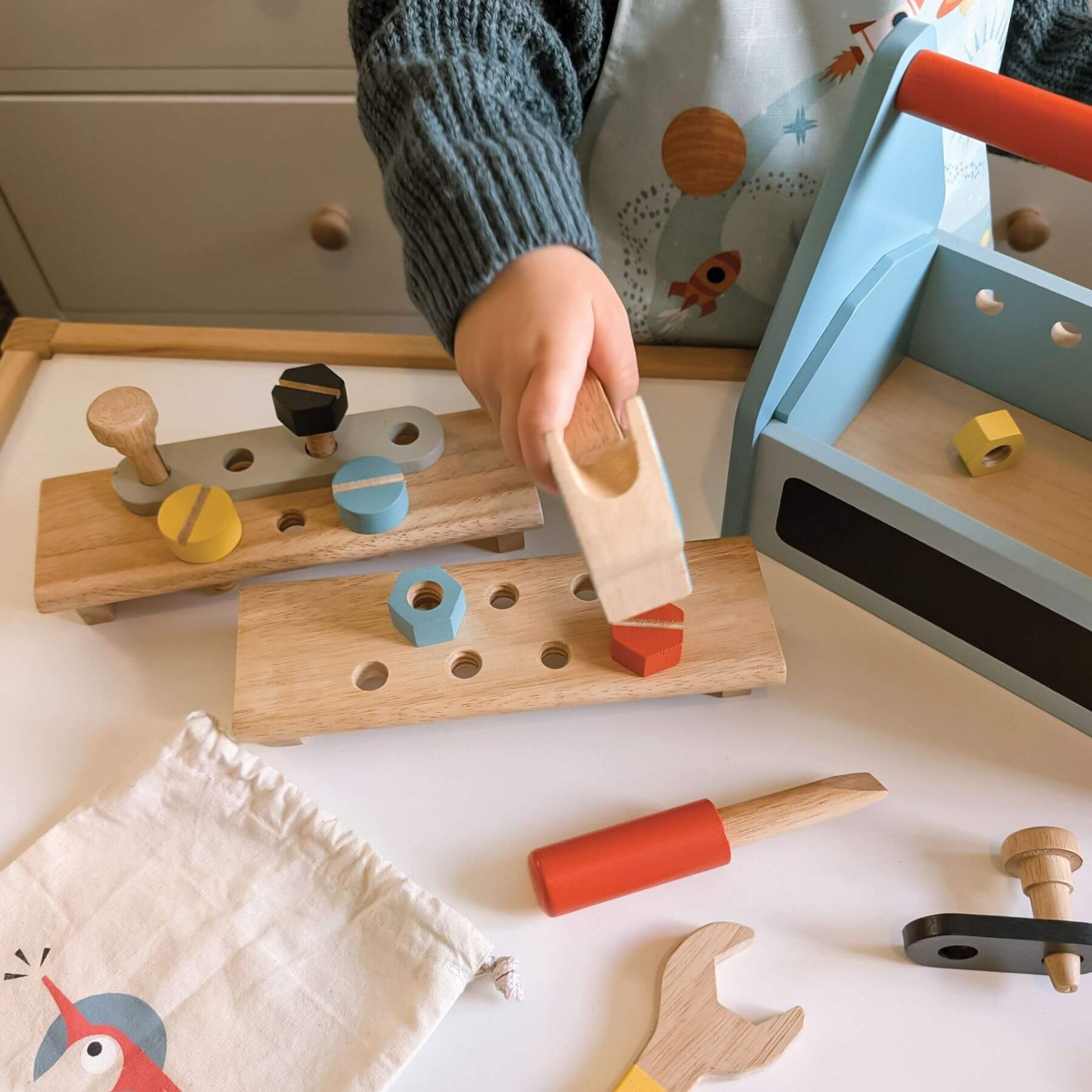 Child playing with wooden tools and shapes on a white surface