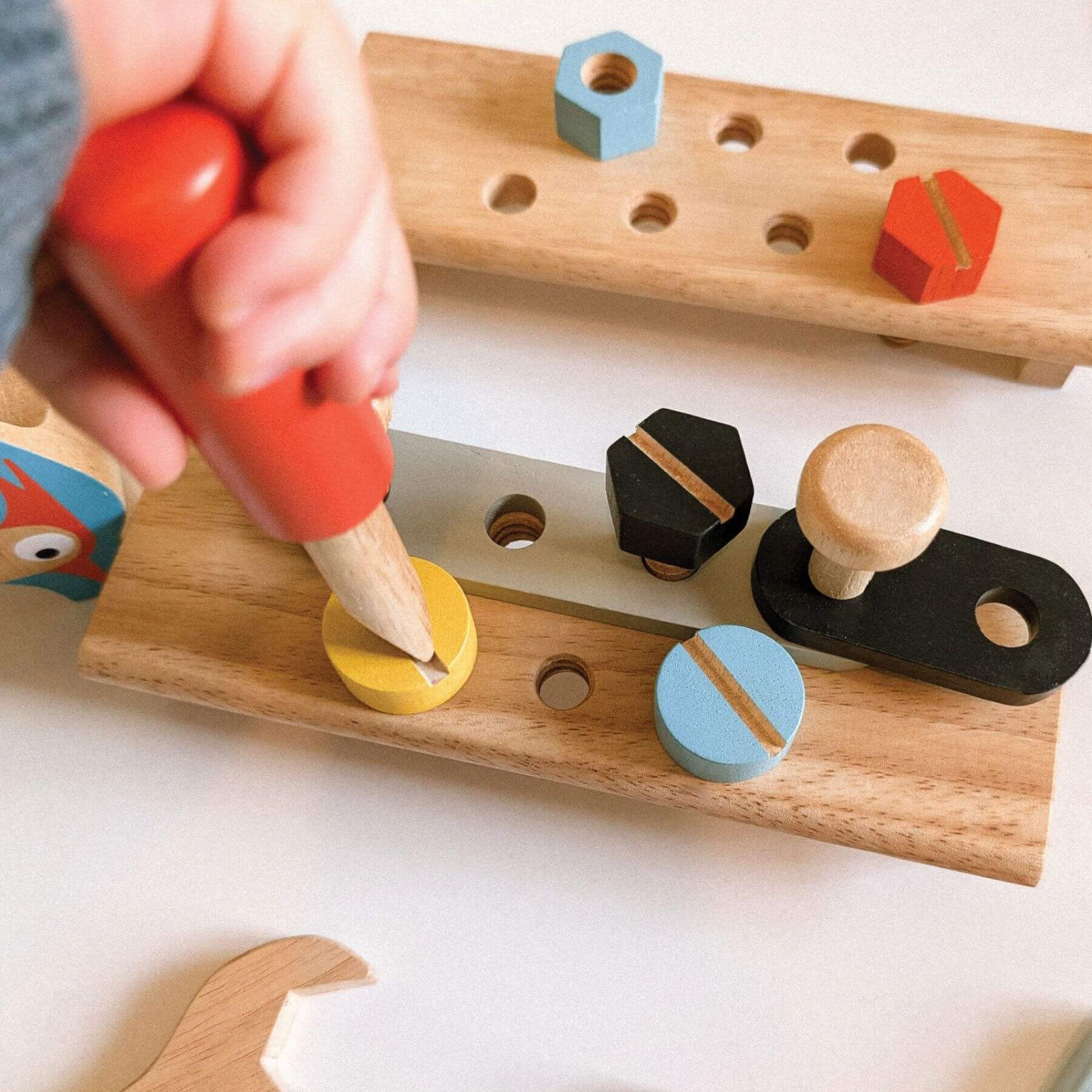 Child playing with a wooden pegboard toy on a white surface