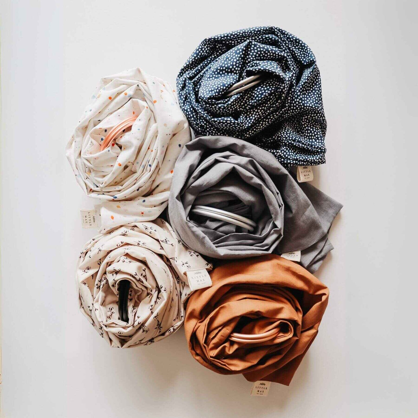 Collection of folded Little Mae & Co Tazzo Ring Sling Carrier in various colors