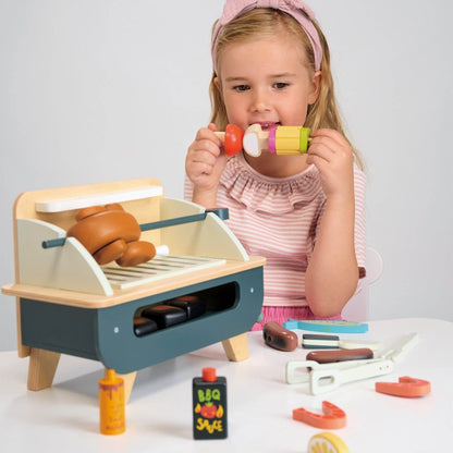 Child playing with Tender Leaf Barbeque Play Set on a white surface