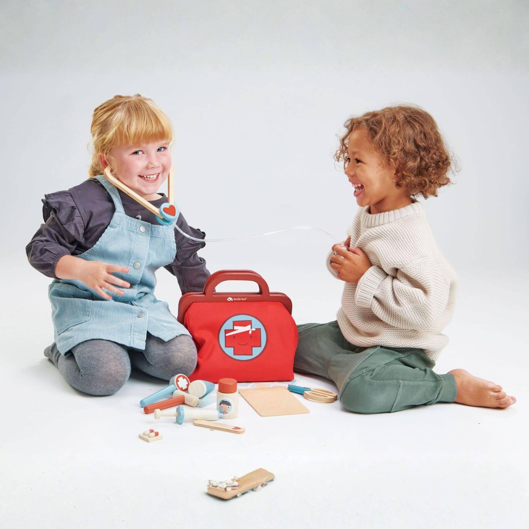 Two children playing with a toy doctor set on a white background