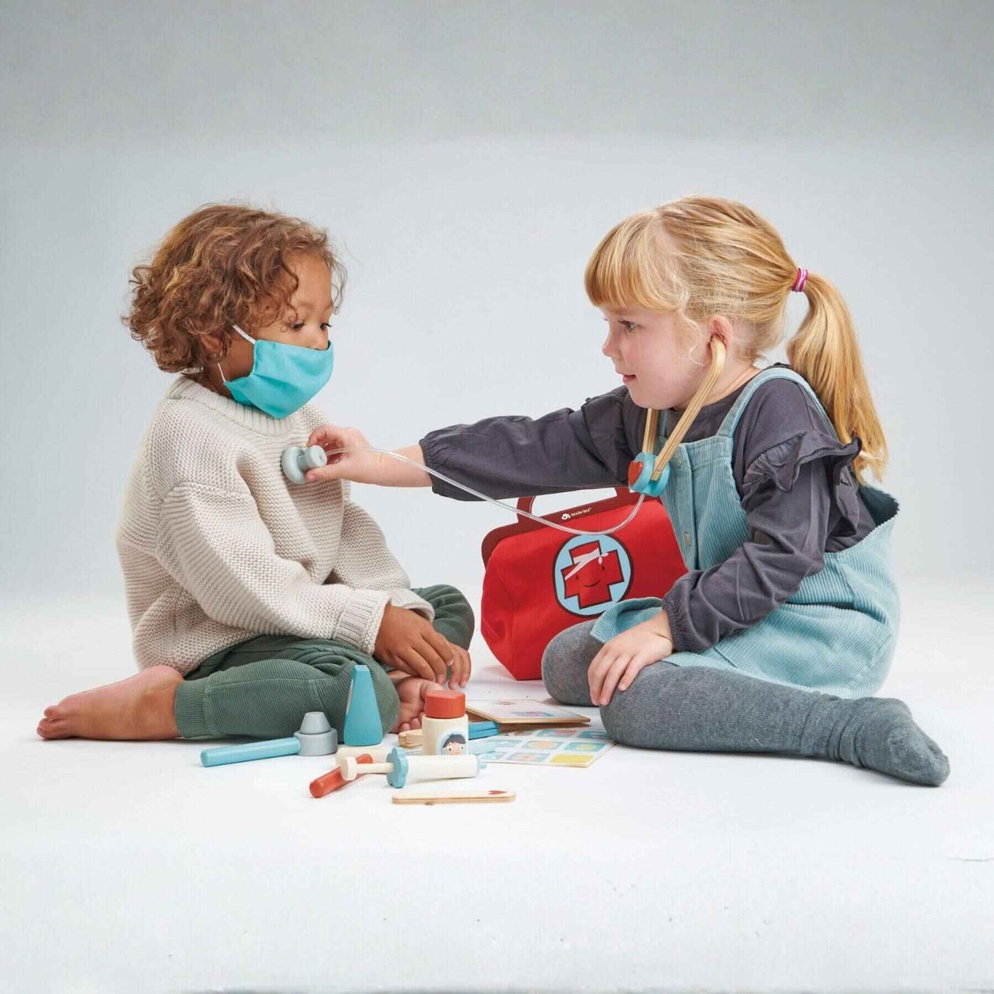 Two children playing with toy medical equipment on a plain background