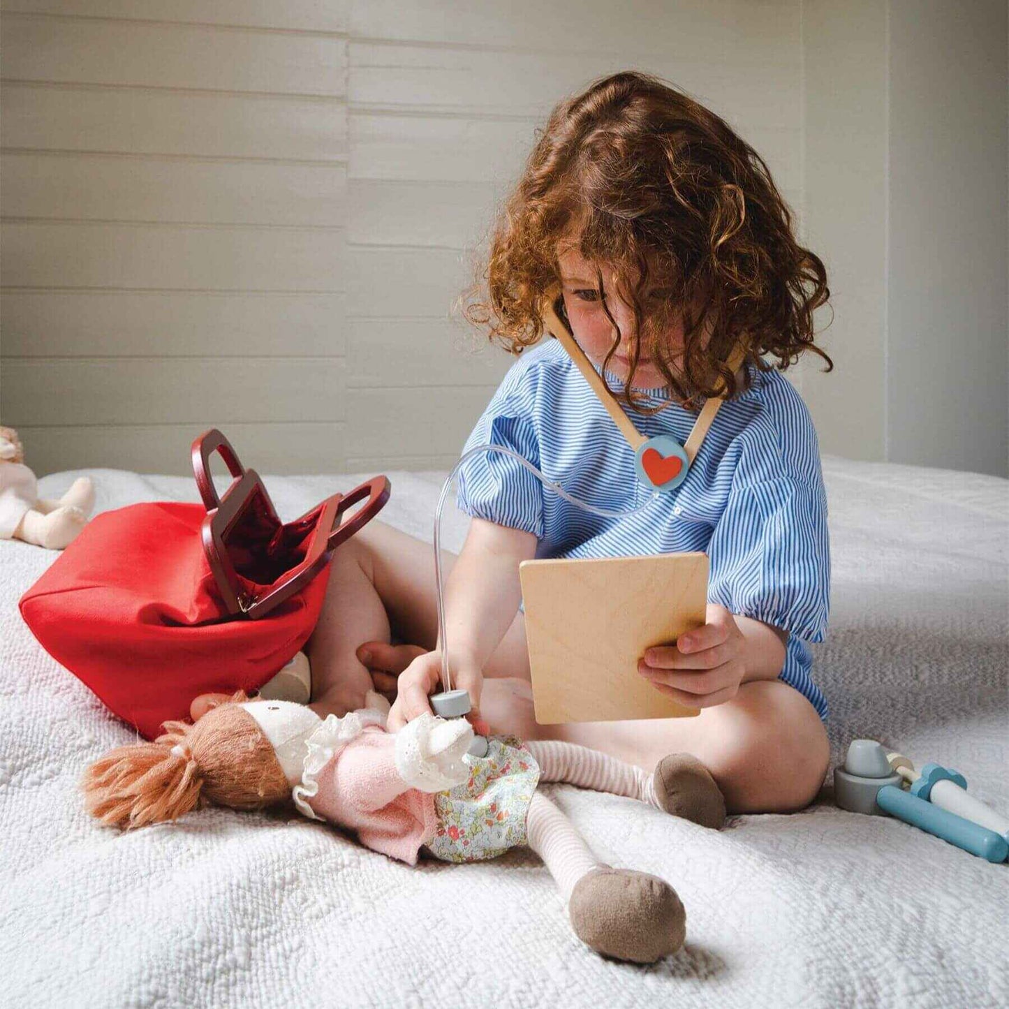 Child sitting on a bed with toys and reading a book