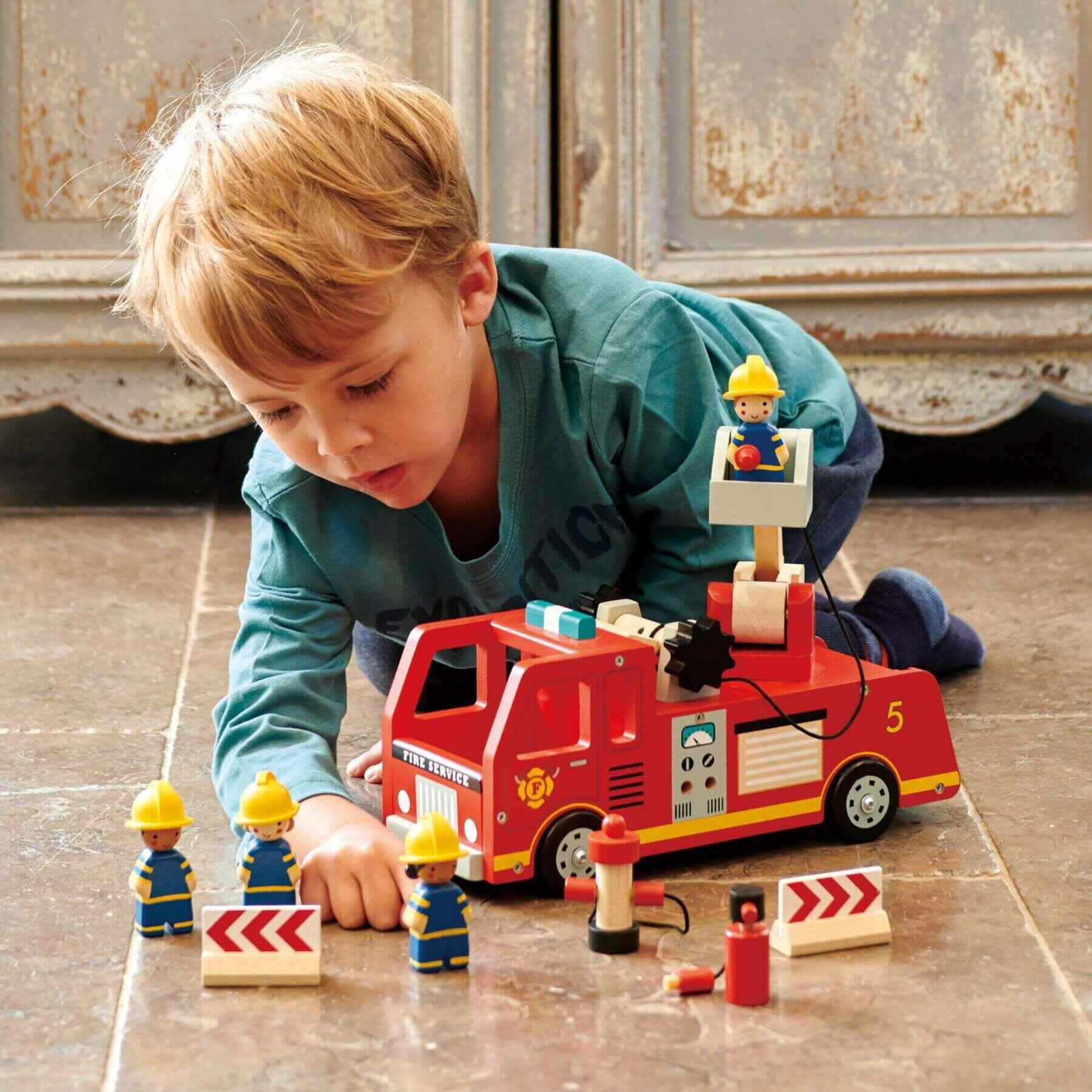 Child playing with Tender Leaf Fire Engine on a wooden floor.