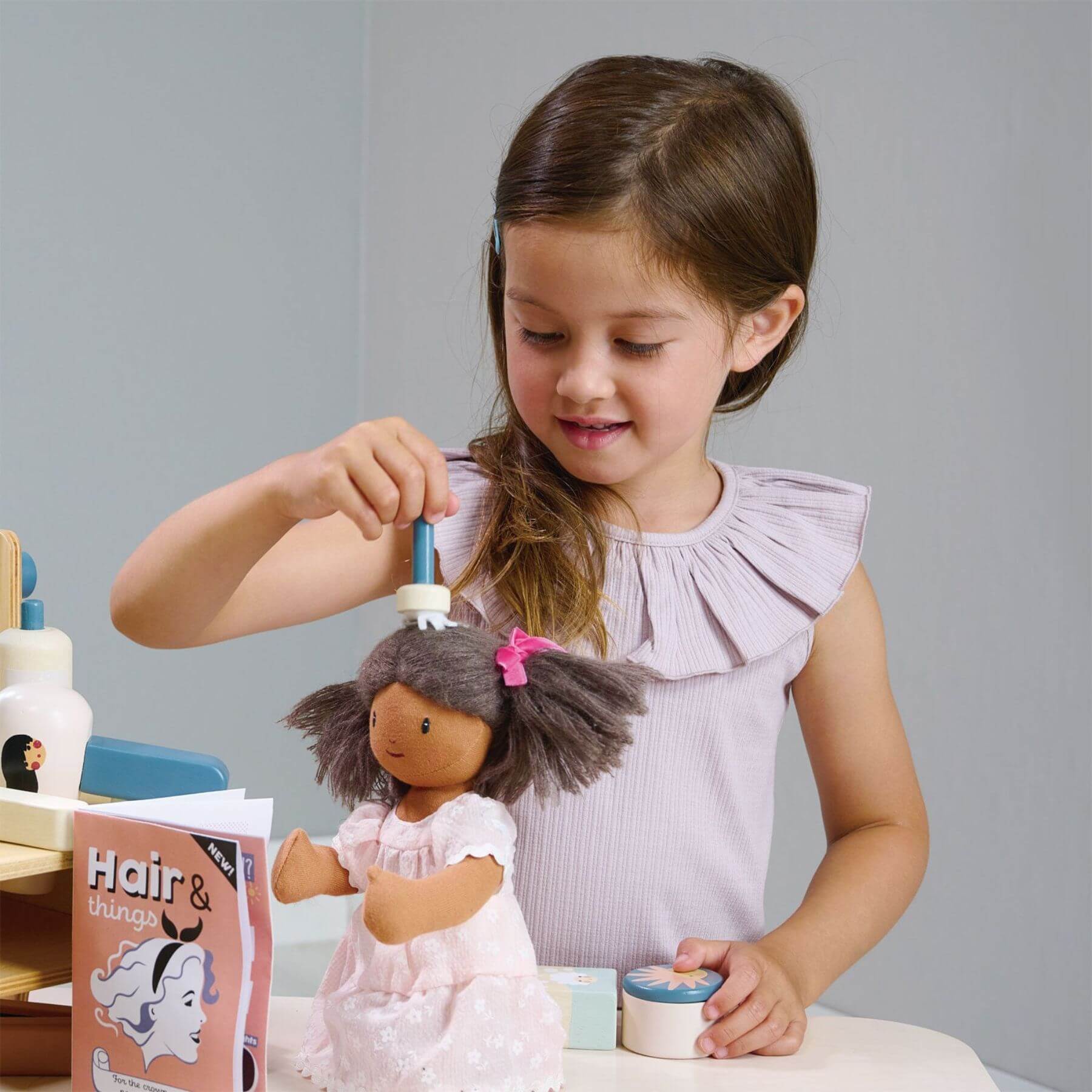 Young girl playing with a doll and Tender Leaf Hair Salon on a table.