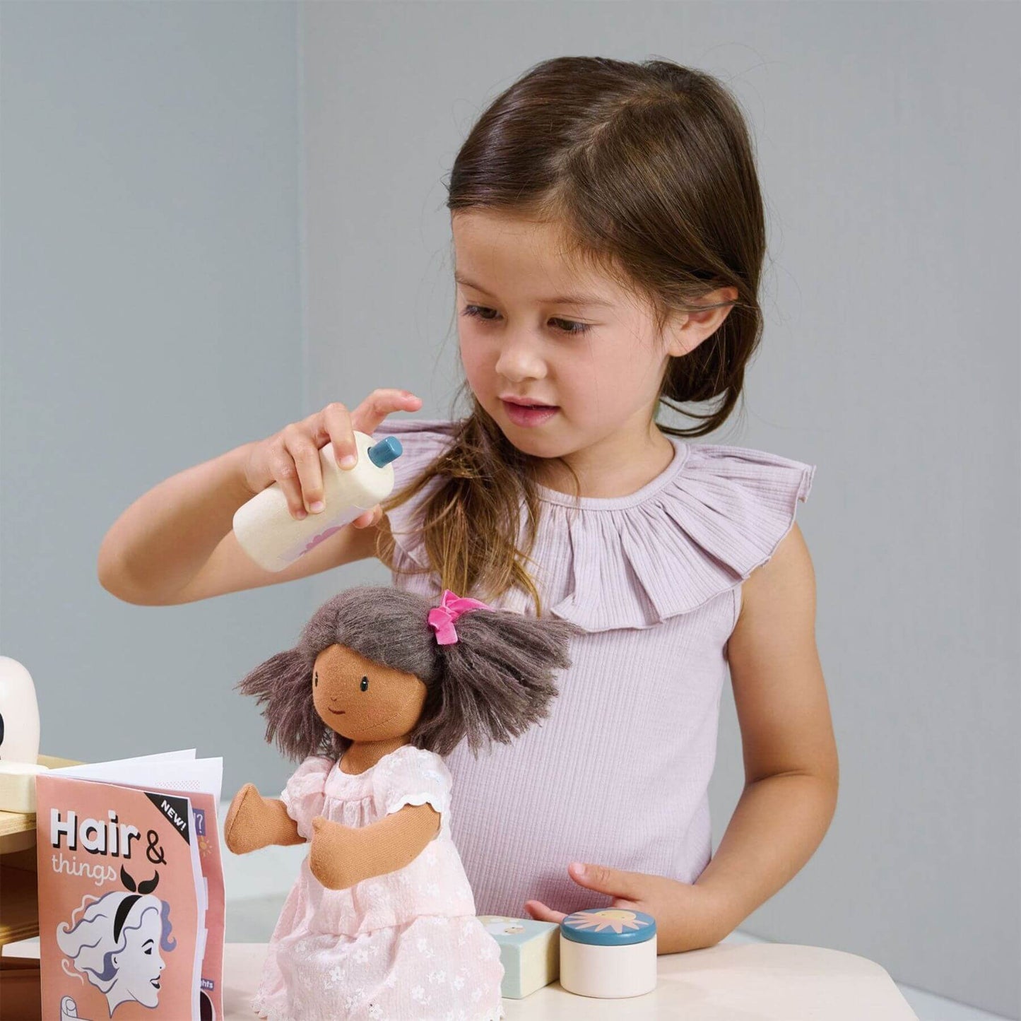 Young girl playing with a doll and Tender Leaf Hair Salon on a table.