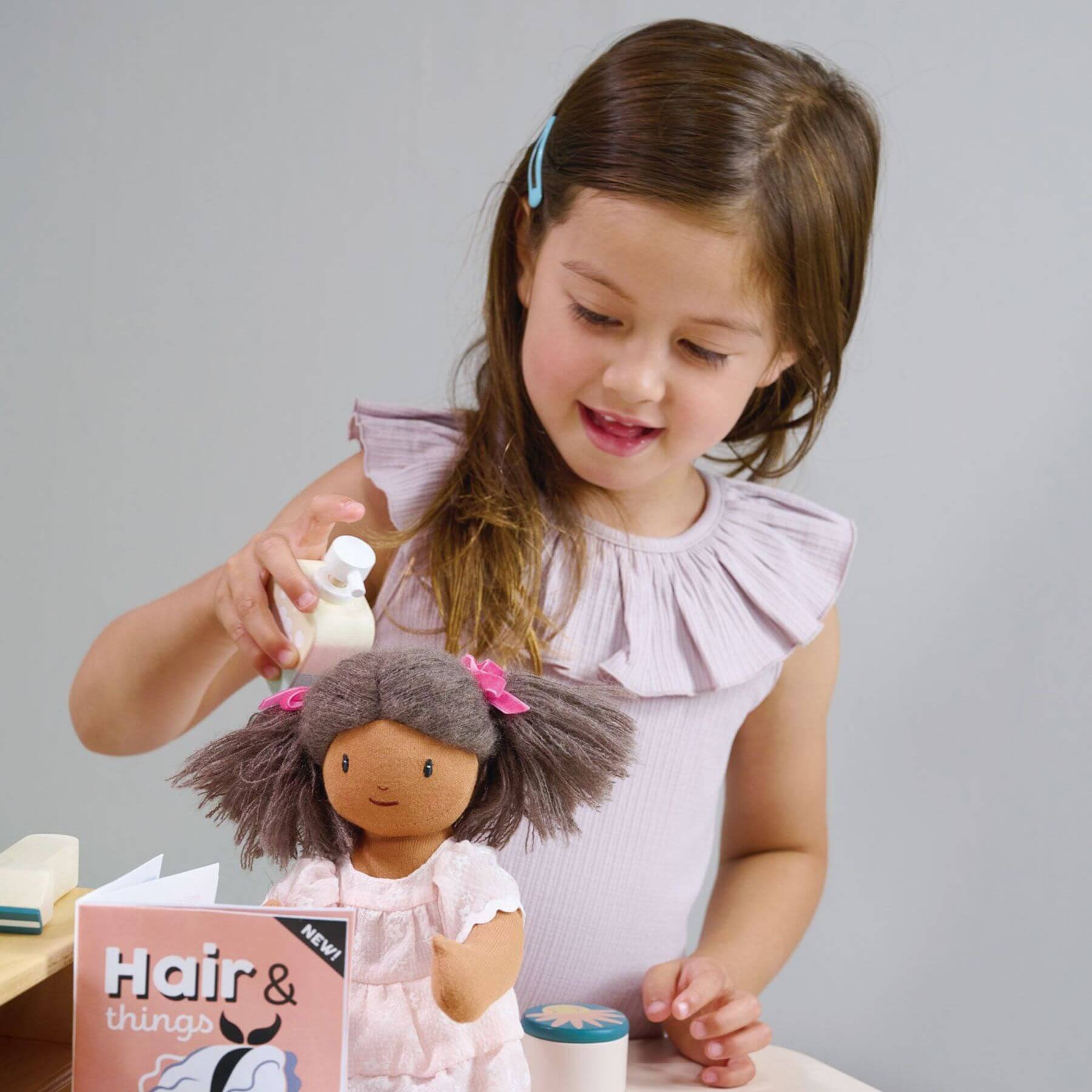 Young girl playing with a doll and Tender Leaf Hair Salon against a gray background