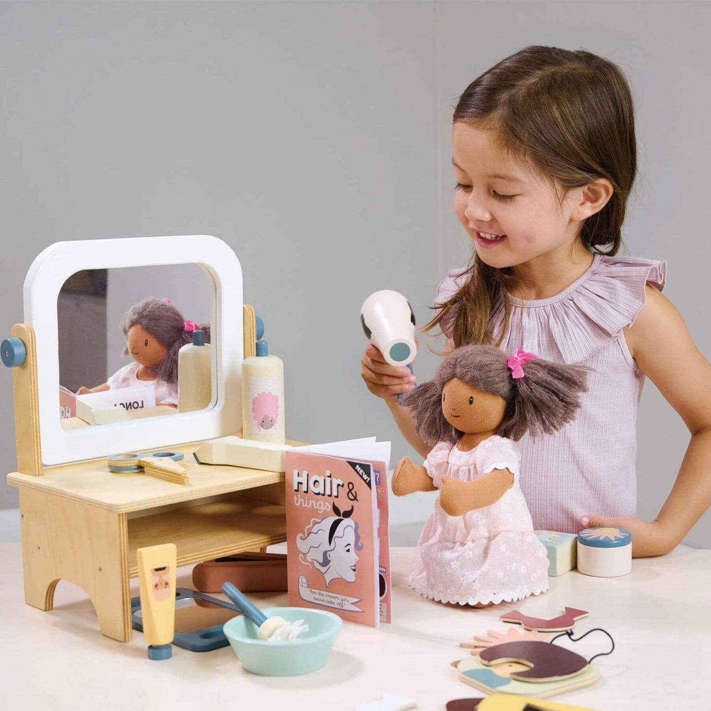 Child playing with a doll and Tender Leaf Hair Salon on a table.