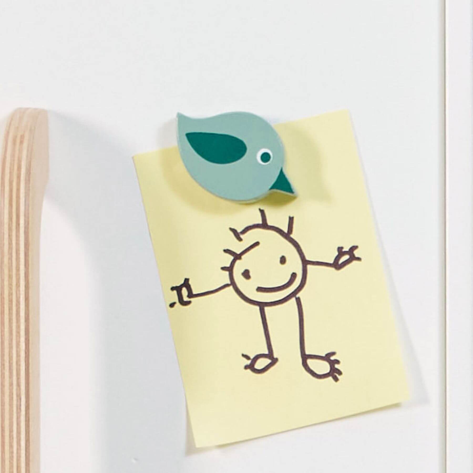Notebook with a stick figure drawing and a green bird-shaped object on Tender Leaf Refrigerator