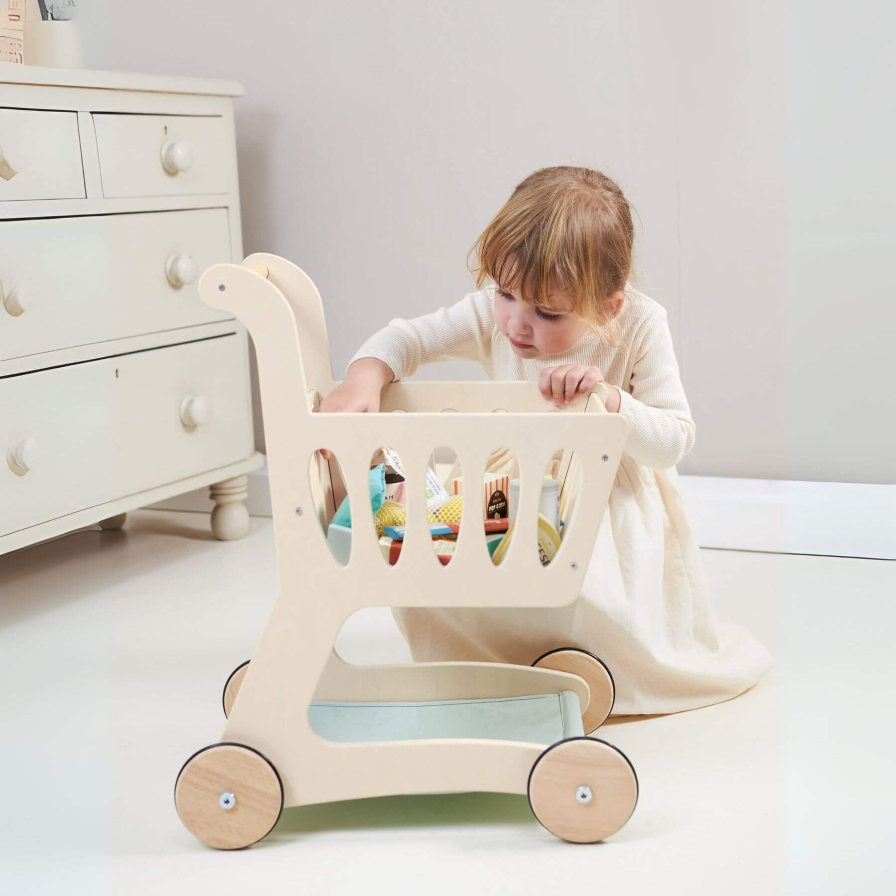 Child playing with Tender Leaf Shopping Cart in a room with a white dresser.
