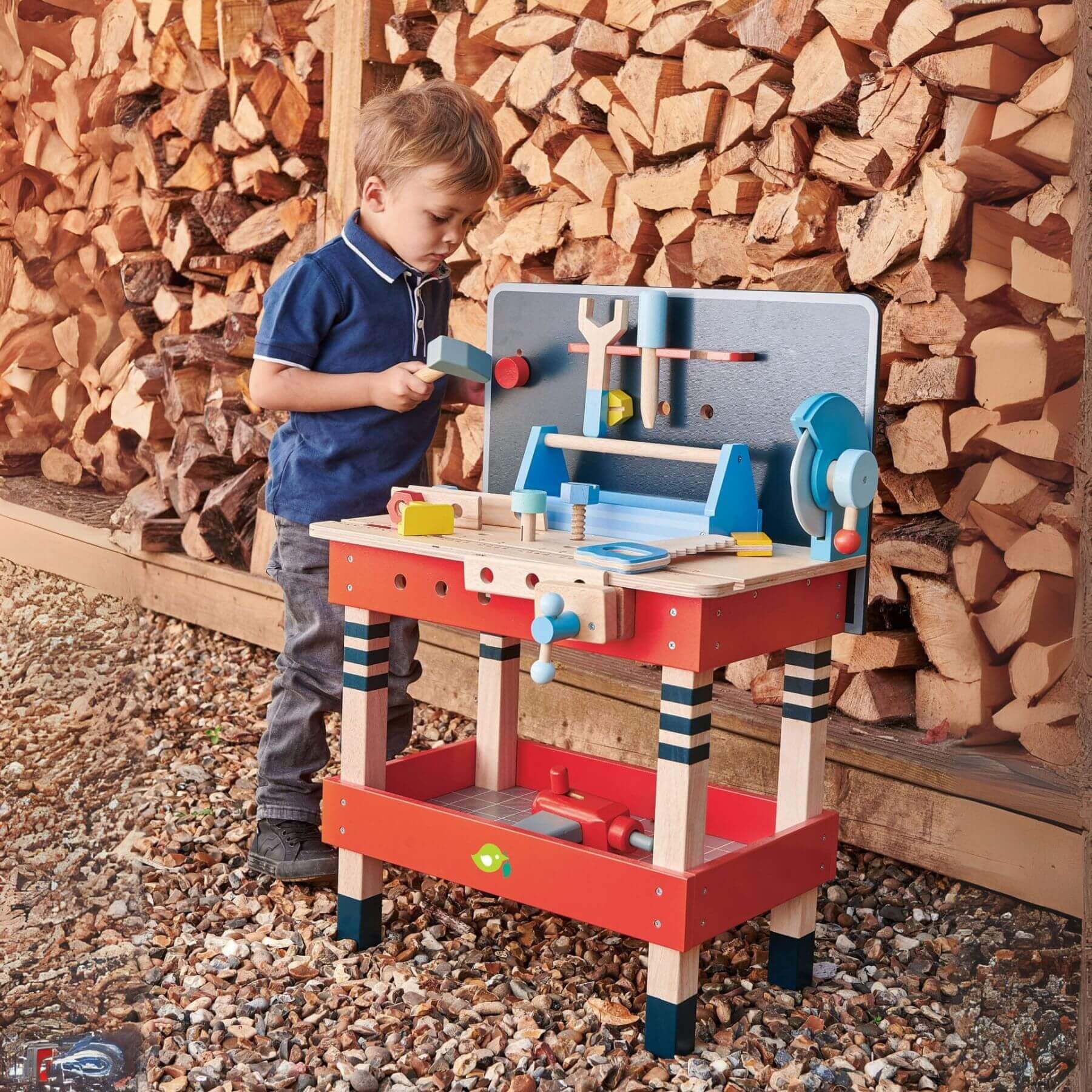 Child playing with Tender Leaf Tool Bench outdoors against a wooden backdrop.