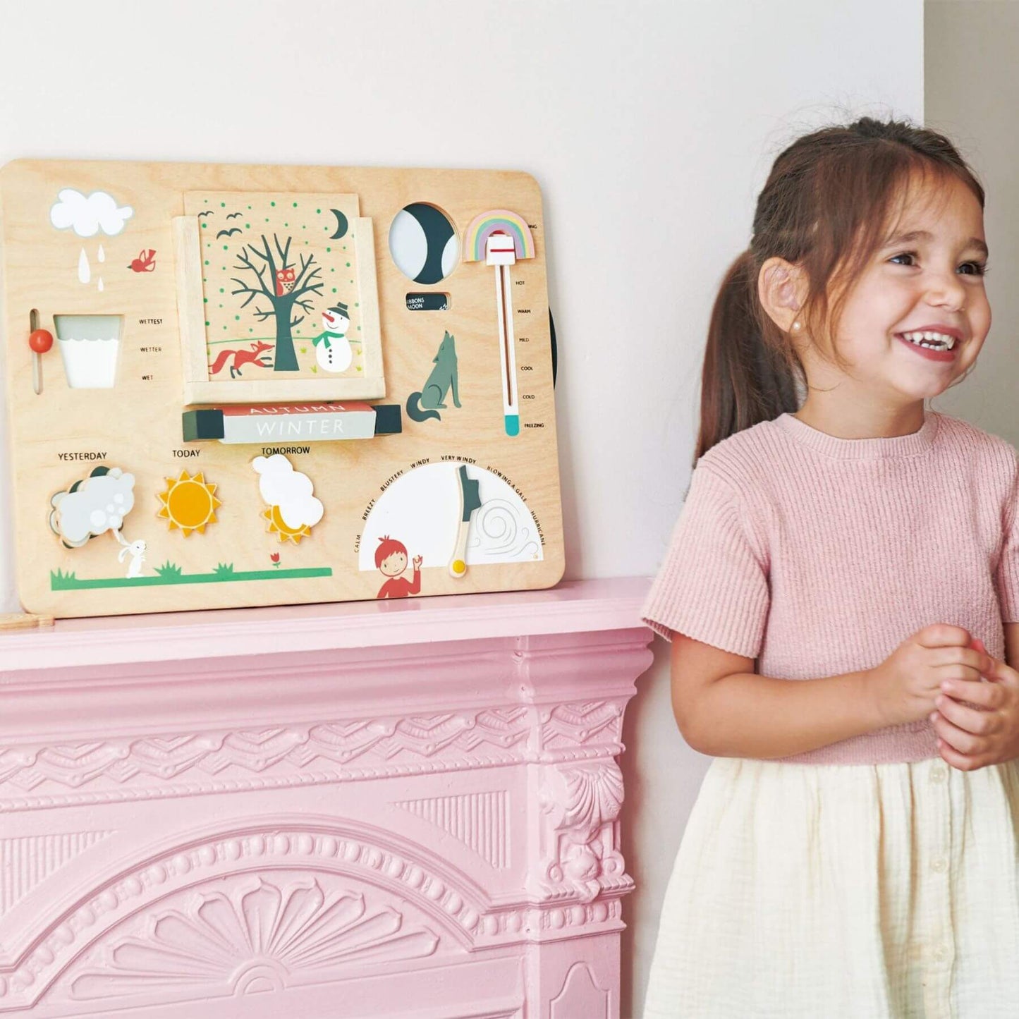 Child standing next to Tender Leaf Weather Watch on a pink fireplace.