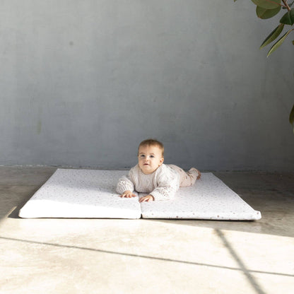 Baby lying on Terrazzo Chalk Organic Cotton Mat in a minimalistic room with a gray wall and wooden floor.