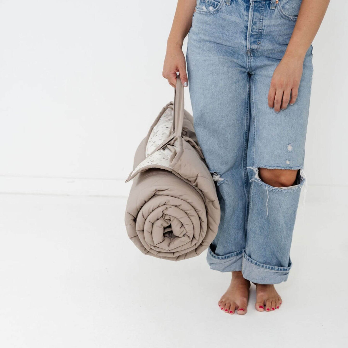 Person holding Toki Kids Terrazzo Chalk Picnic Blanket wearing ripped jeans on a white background