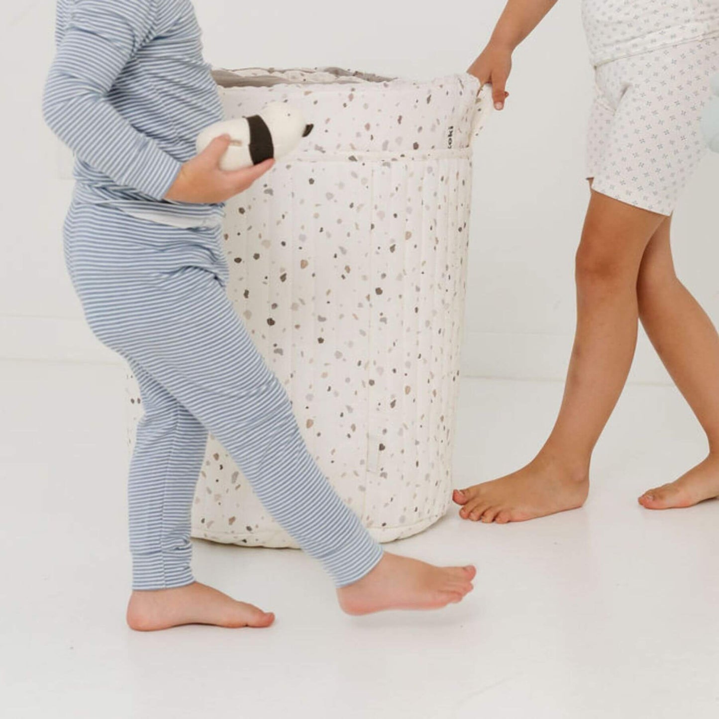 Child wearing blue striped pajama pants holding a stuffed animal on a white background