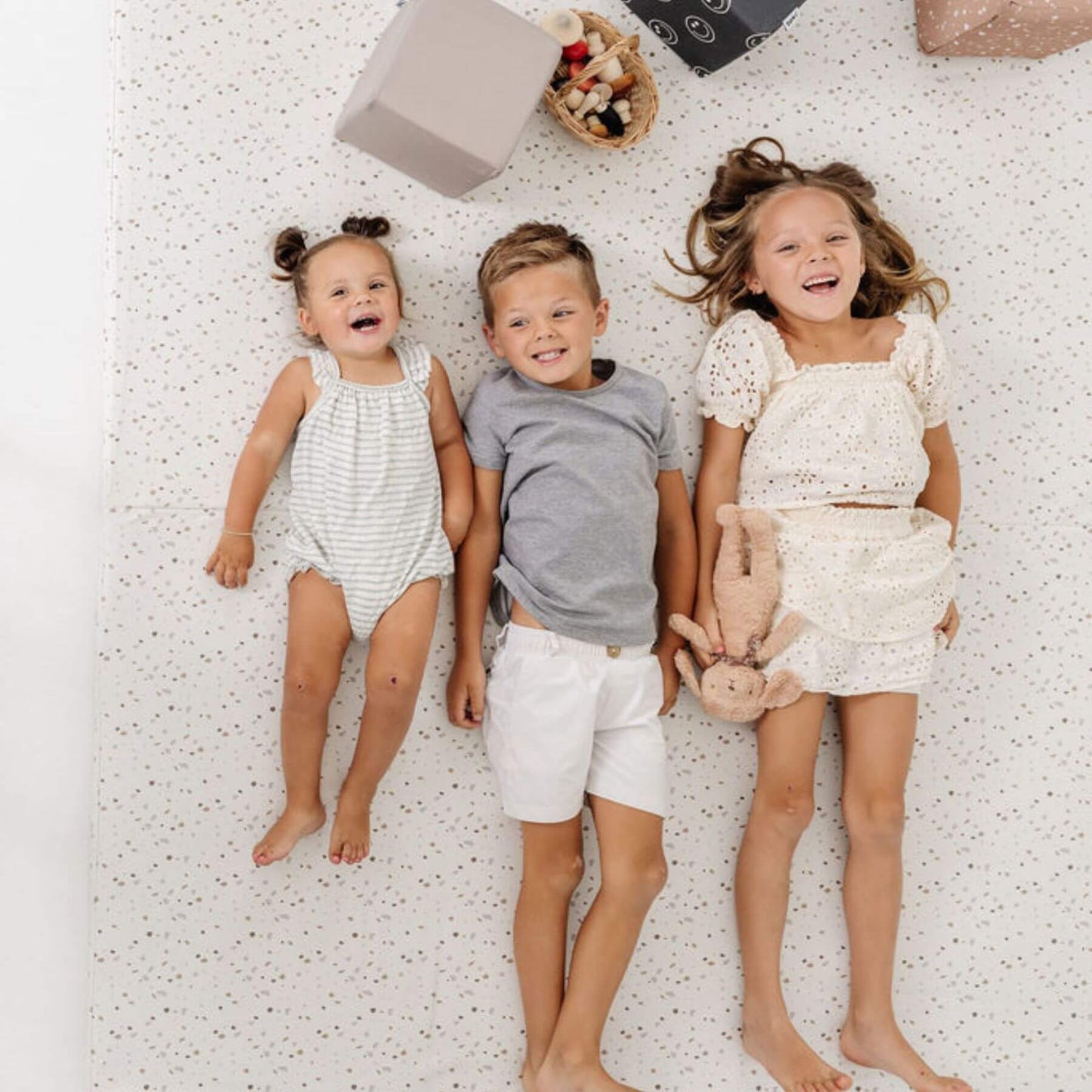 Three kids lying on Toki Kids Terrazzo Chalk Vegan Leather Mat