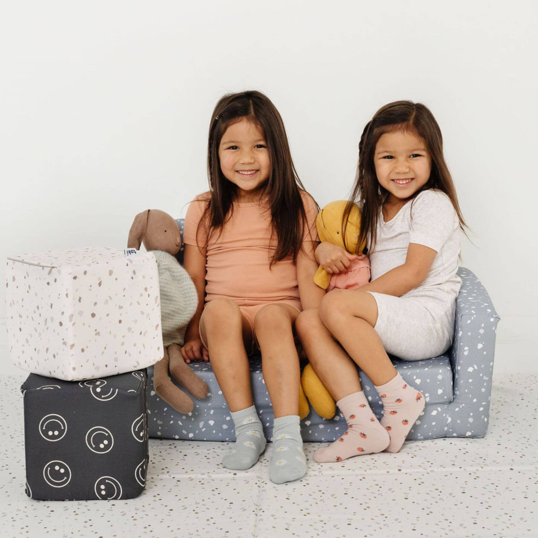 Two girls sitting on play sofa on Toki Kids Terrazzo Chalk Vegan Leather Mat
