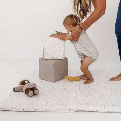 Hand holding a baby playing toys on Toki Kids Terrazzo Chalk Vegan Leather Mat