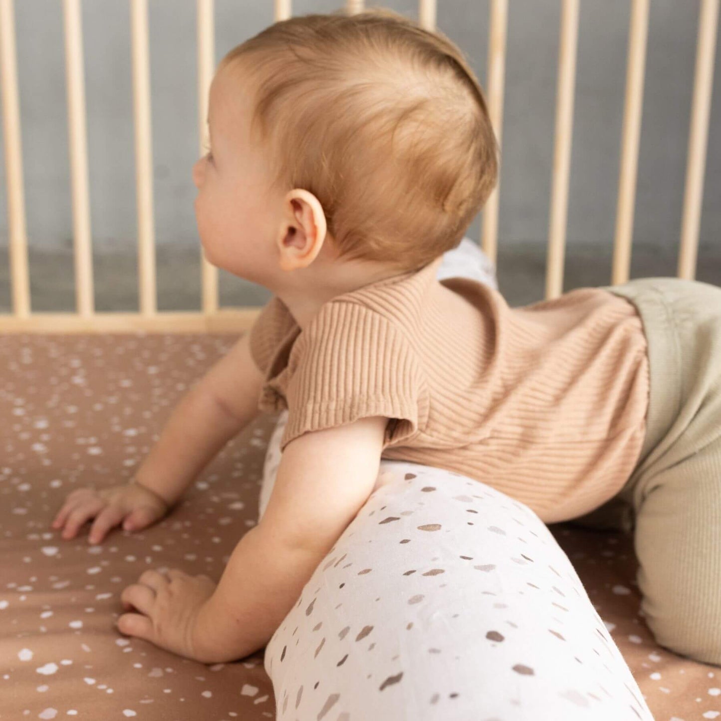 Baby in a beige outfit crawling on Terrazzo Clay Organic Cotton Mat with white patterns.