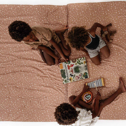 Three children sitting on Terrazzo Clay Organic Cotton Mat with books and toys around them.