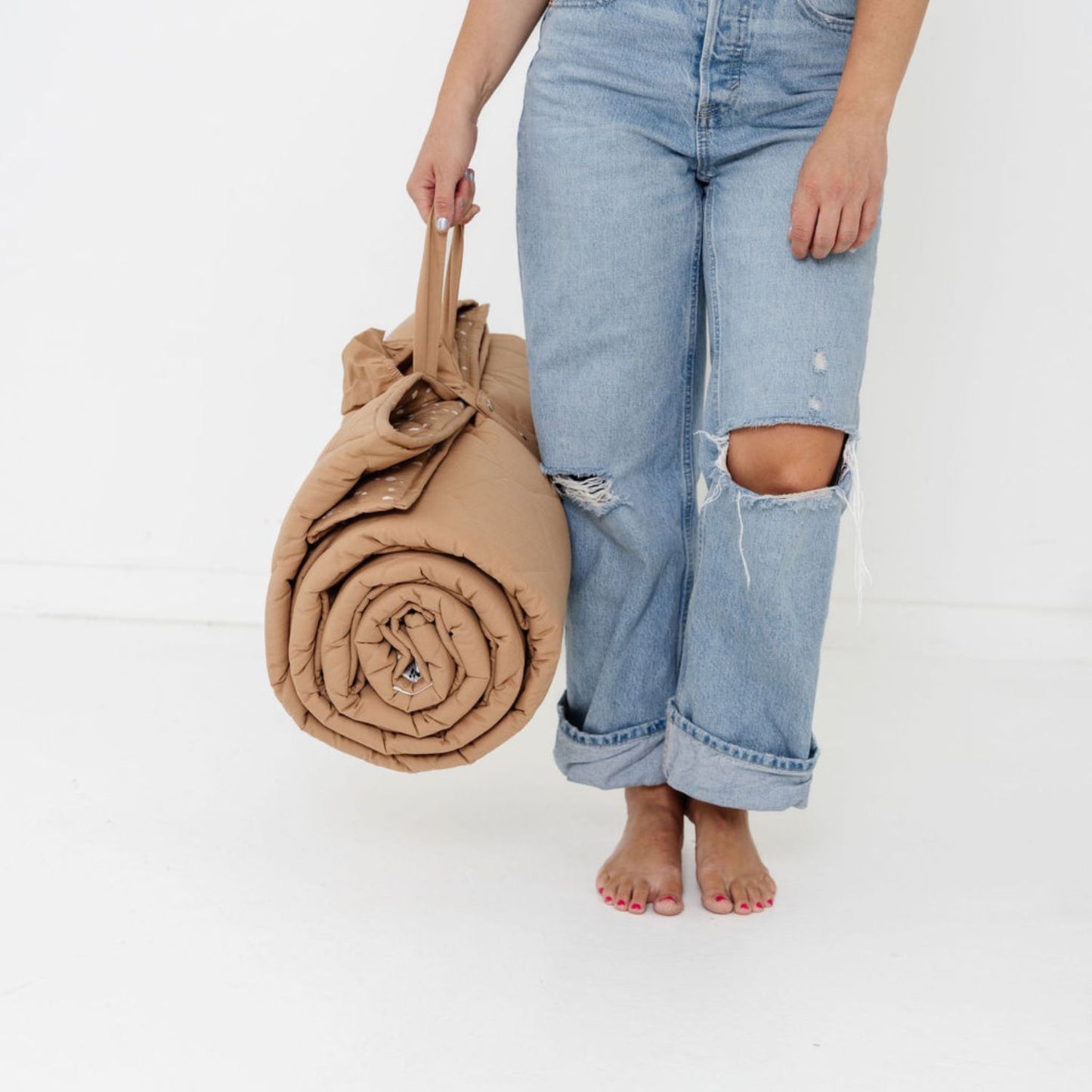 Person holding a rolled-up beige blanket wearing light blue jeans on a white background
