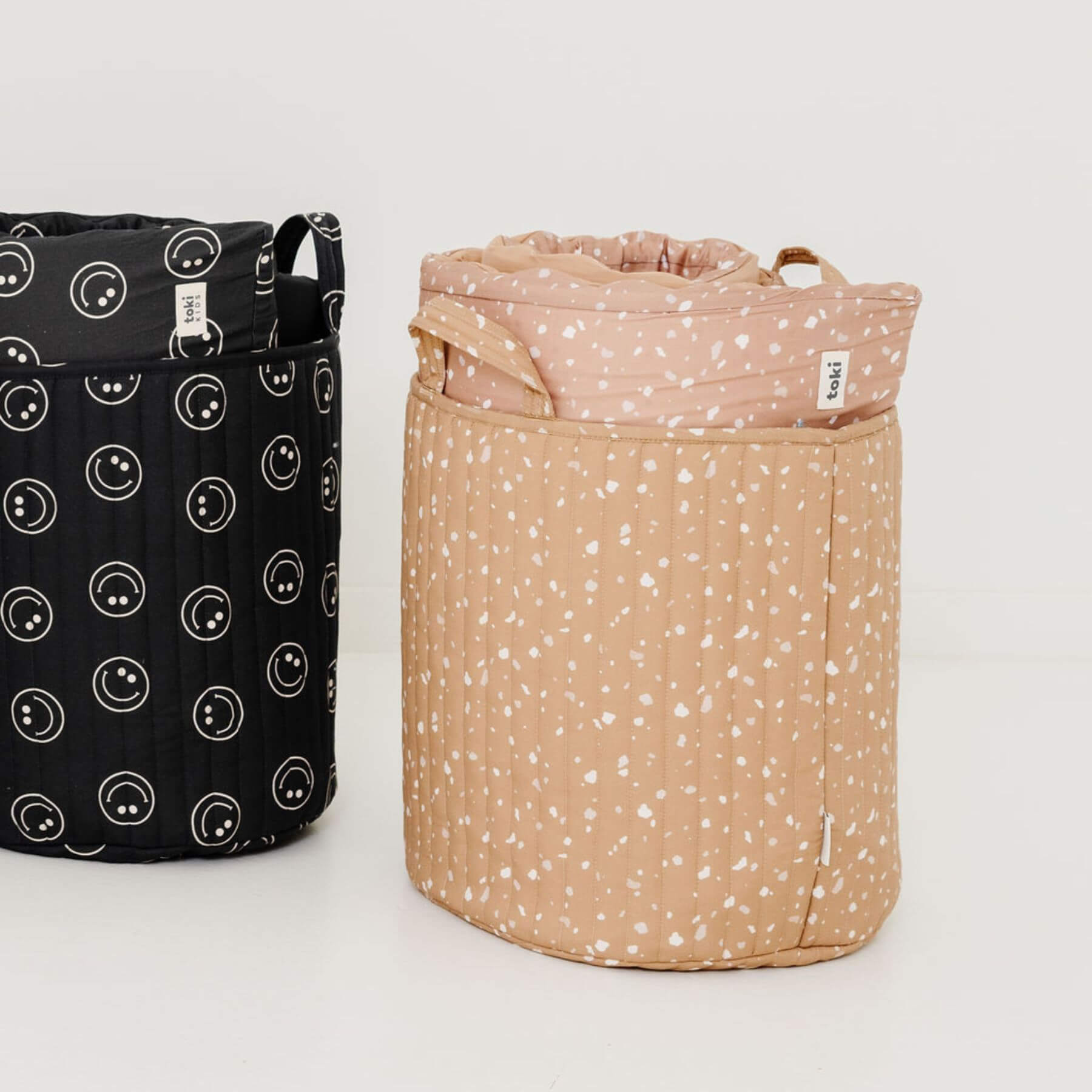 Two fabric baskets, one black with white patterns and the other beige with white speckles, on a light gray background.