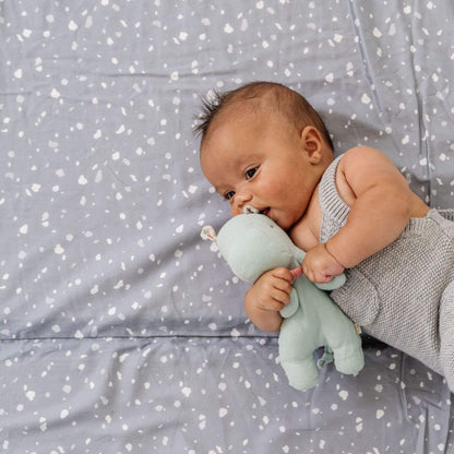 Baby holding a green plush toy on Terrazzo Slate Organic Cotton Mat