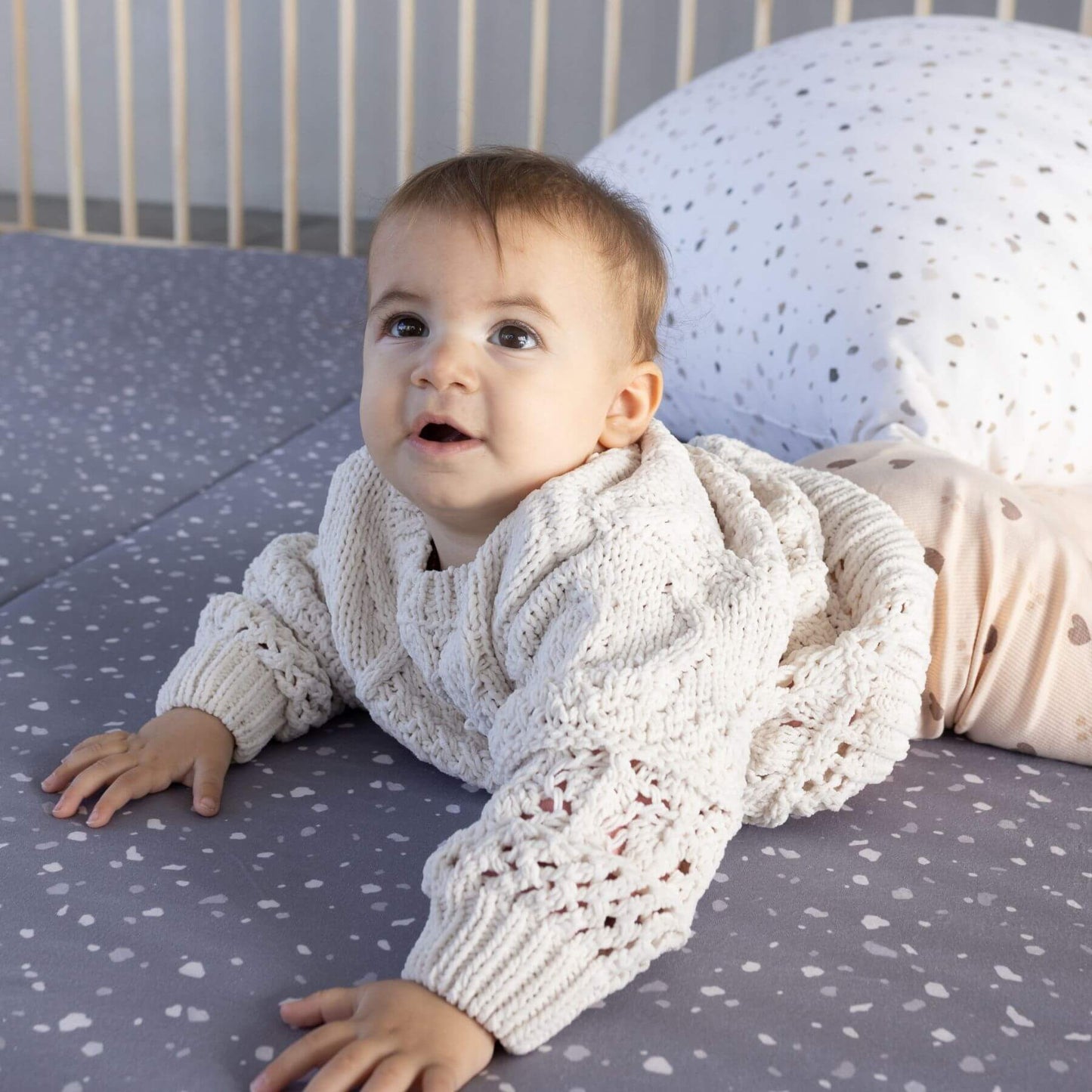 Baby wearing a white knit sweater lying on Terrazzo Slate Organic Cotton Mat
