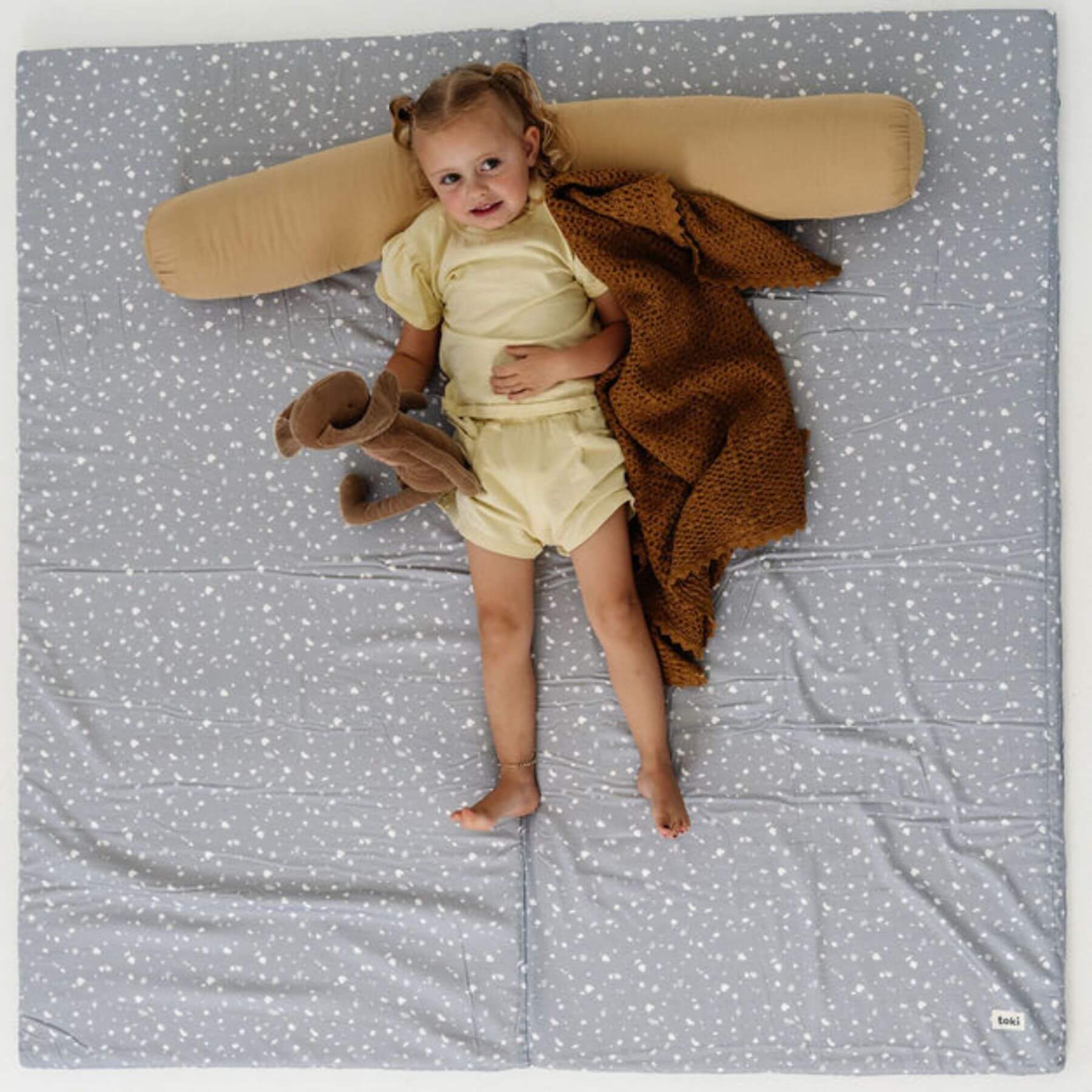 Child lying on Terrazzo Slate Organic Cotton Mat, wearing a yellow outfit.