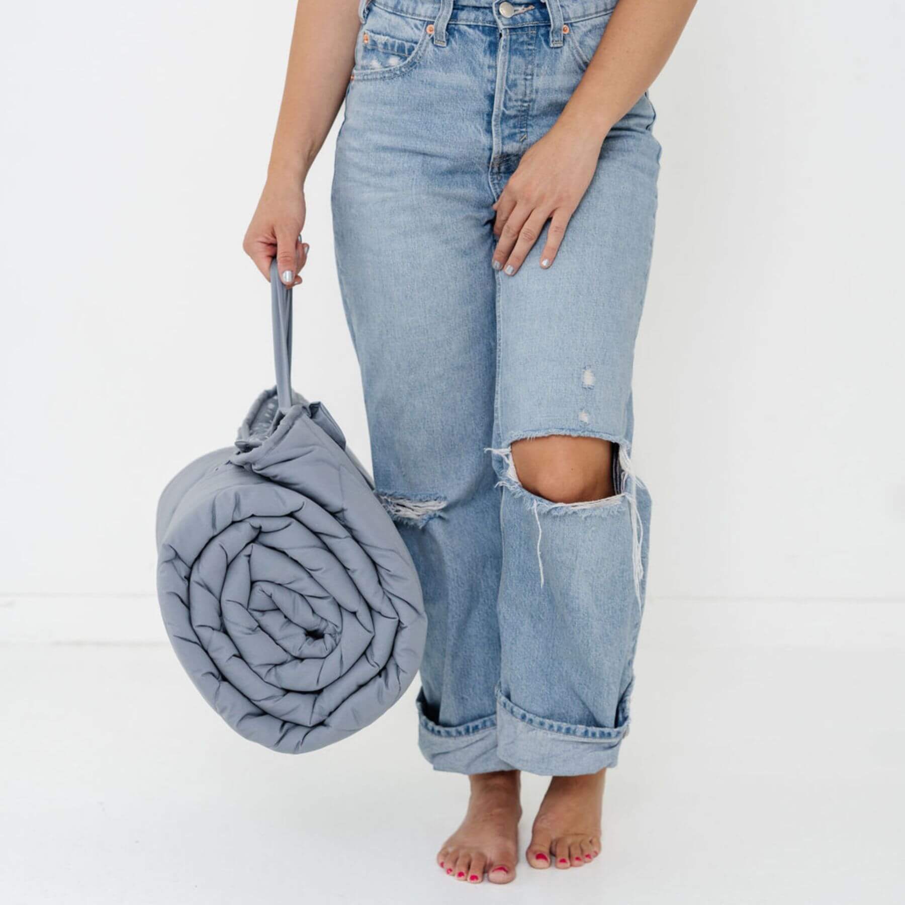 Person wearing light blue jeans holding a rolled-up Toki Kids Terrazzo Slate Picnic Blanket