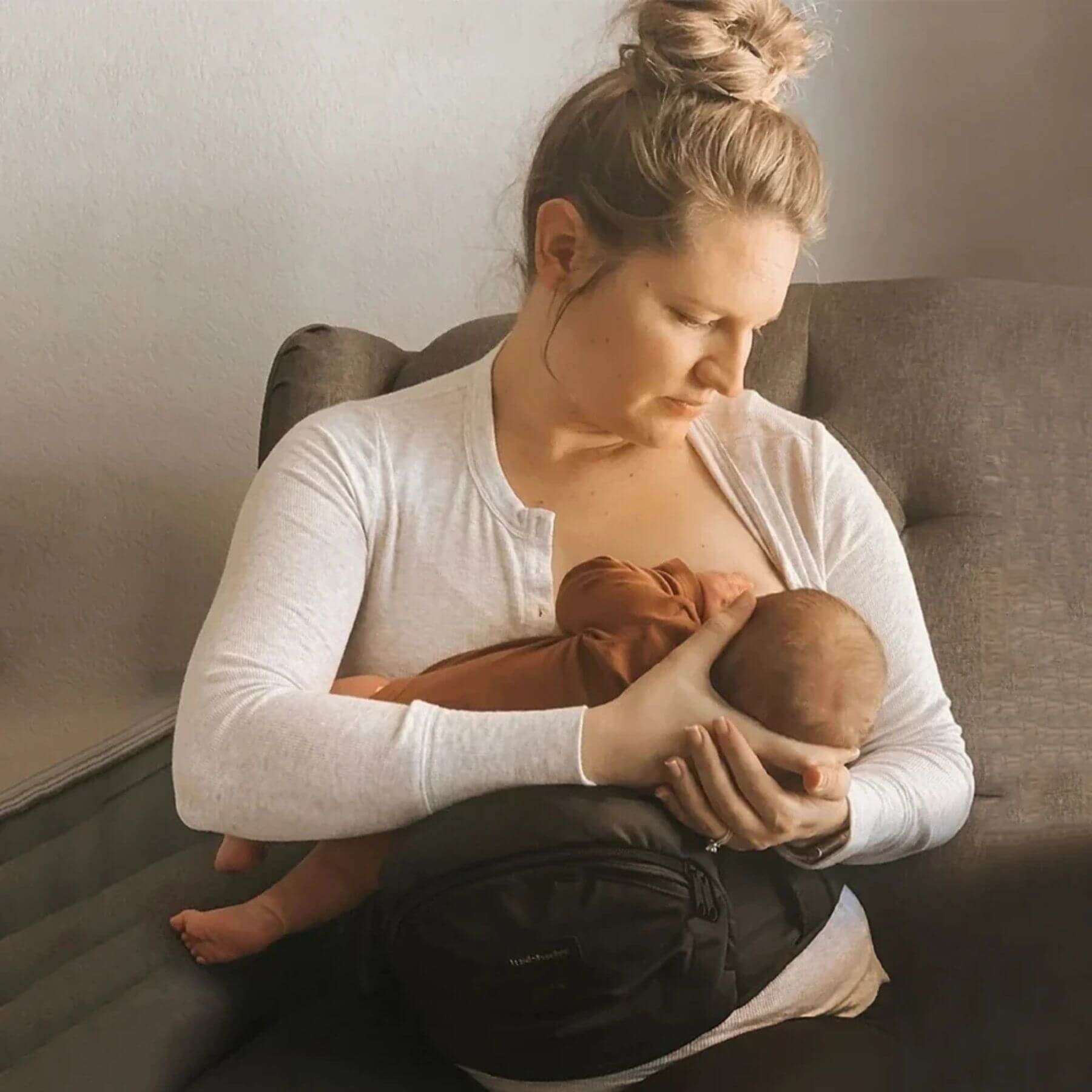 Woman breastfeeding a baby in Man holding a baby in The Tushbaby Hip Carrier - Black on a couch