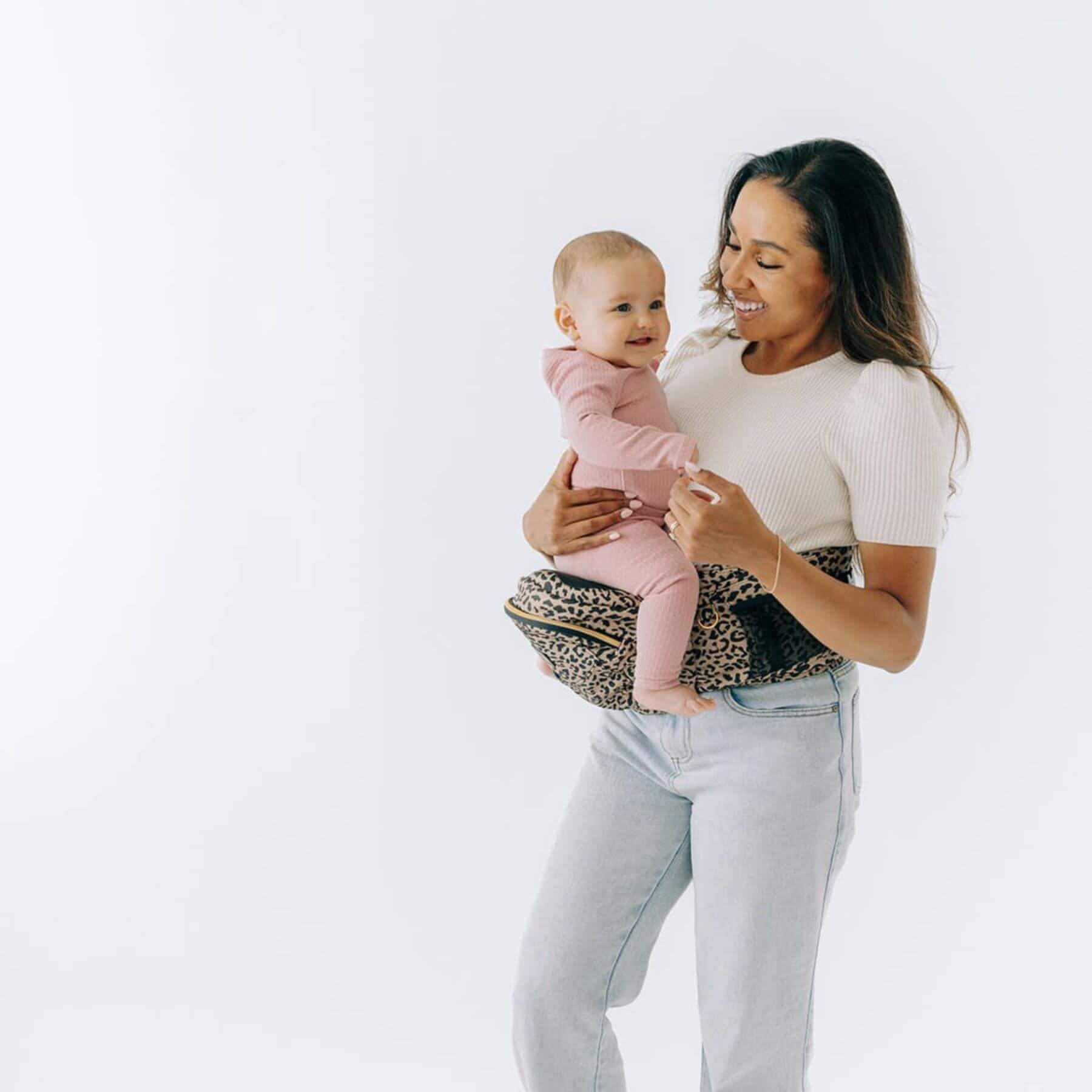Woman holding a baby with The Tushbaby Hip Carrier - Cheetah