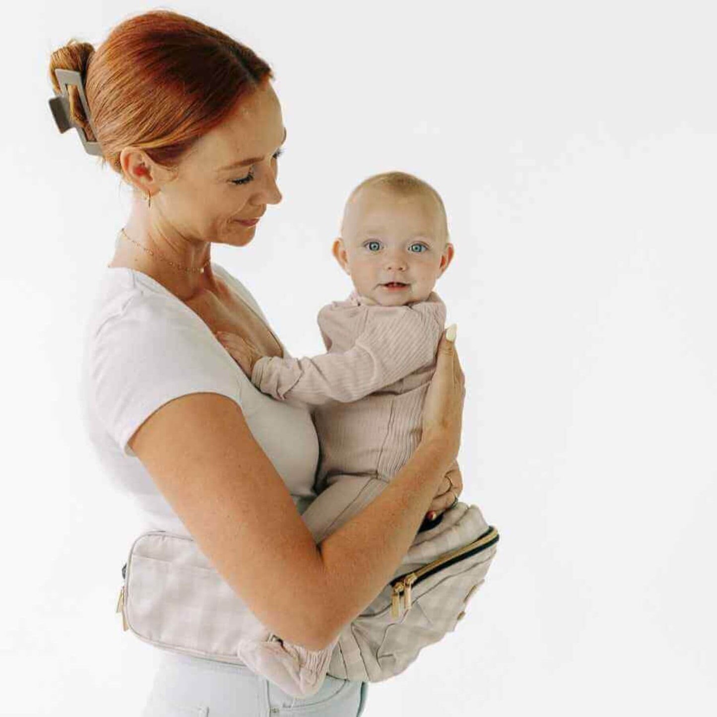 Woman holding a baby in The Tushbaby Hip Carrier - Gingham