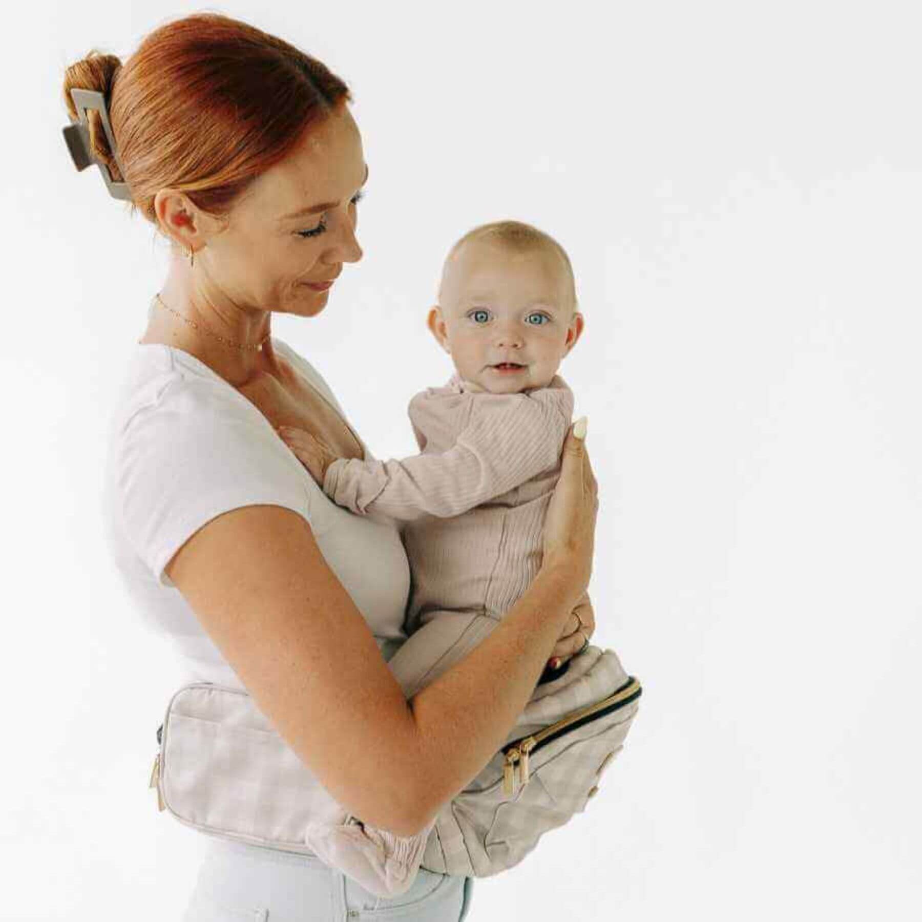 Woman holding a baby in The Tushbaby Hip Carrier - Gingham