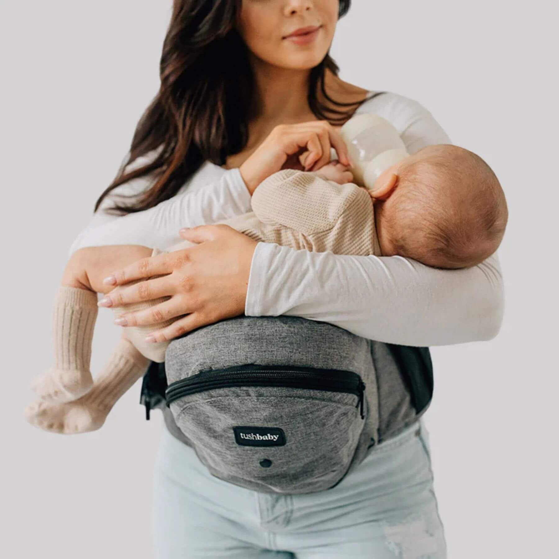 Woman holding a baby in The Tushbaby Hip Carrier - Grey
