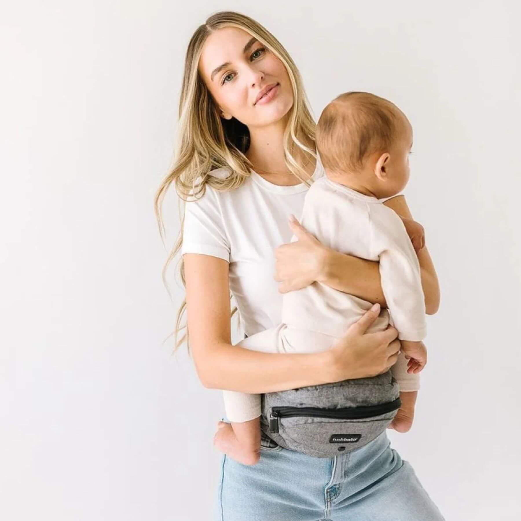 Woman holding a baby in The Tushbaby Hip Carrier - Grey