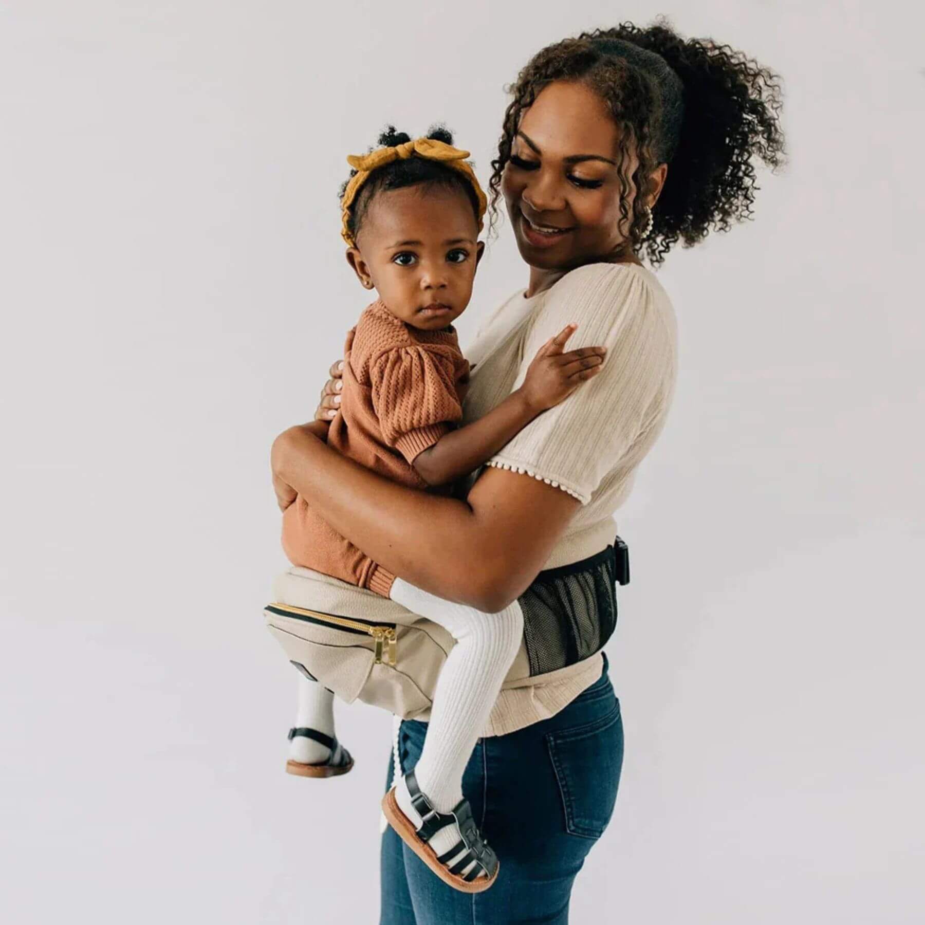 Woman holding a child in The Tushbaby Hip Carrier - Vegan Leather Cognac